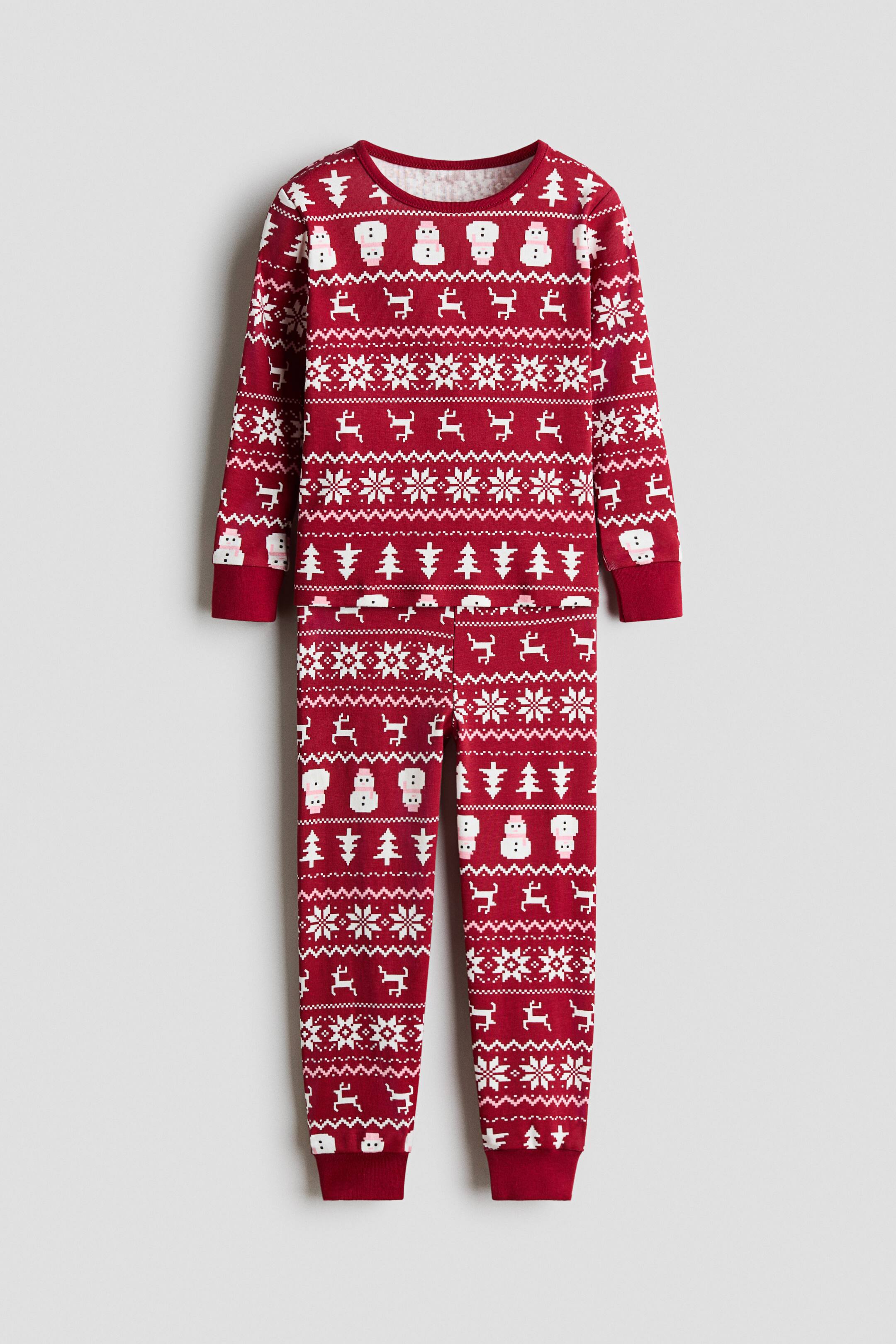 Voir une image plus grande: Un ensemble de pyjama rouge, présenté de face, comprend un haut à manches longues assorti et un pantalon avec un imprimé des Fêtes blanc et rose représentant des bonshommes de neige, des rennes, des flocons de neige et des sapins. Le haut présente un col rond et des poignets côtelés, tandis que le pantalon coordonné affiche des ourlets côtelés.