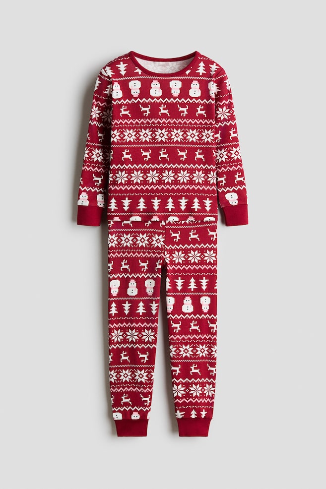 A front-facing red pyjama set is featuring a matching long-sleeved top and pants with a white and pink holiday print of snowmen, reindeer, snowflakes, and pine trees. The top is showing a round neckline and ribbed cuffs, while the coordinating pants are displaying ribbed hems. - 1