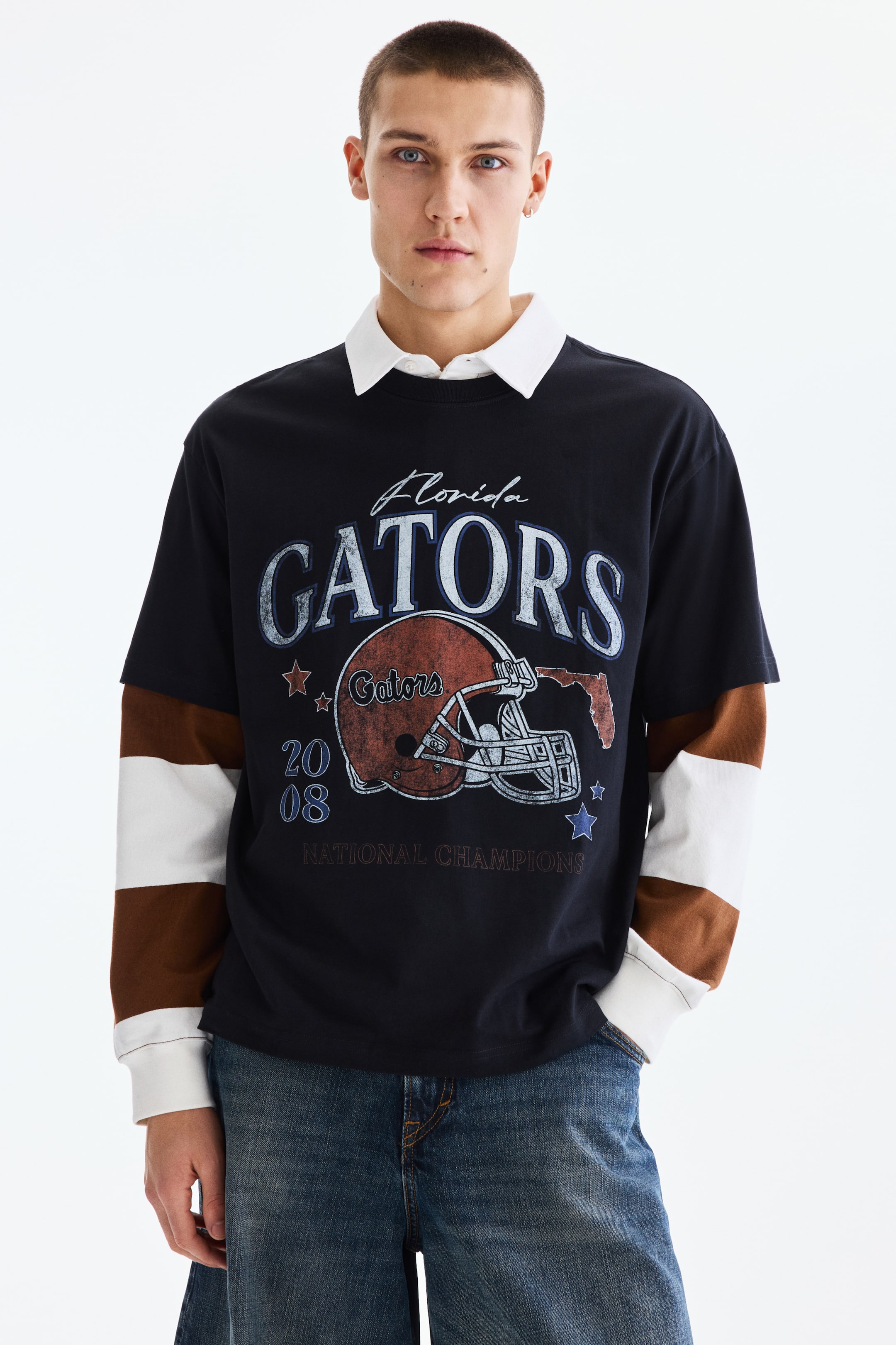 View larger image: This layered-look top showcases a dark navy short-sleeved t-shirt featuring a 'Florida GATORS 2008 NATIONAL CHAMPIONS' graphic on the front. It reveals a white collared shirt underneath and long sleeves with white and brown horizontal stripes.