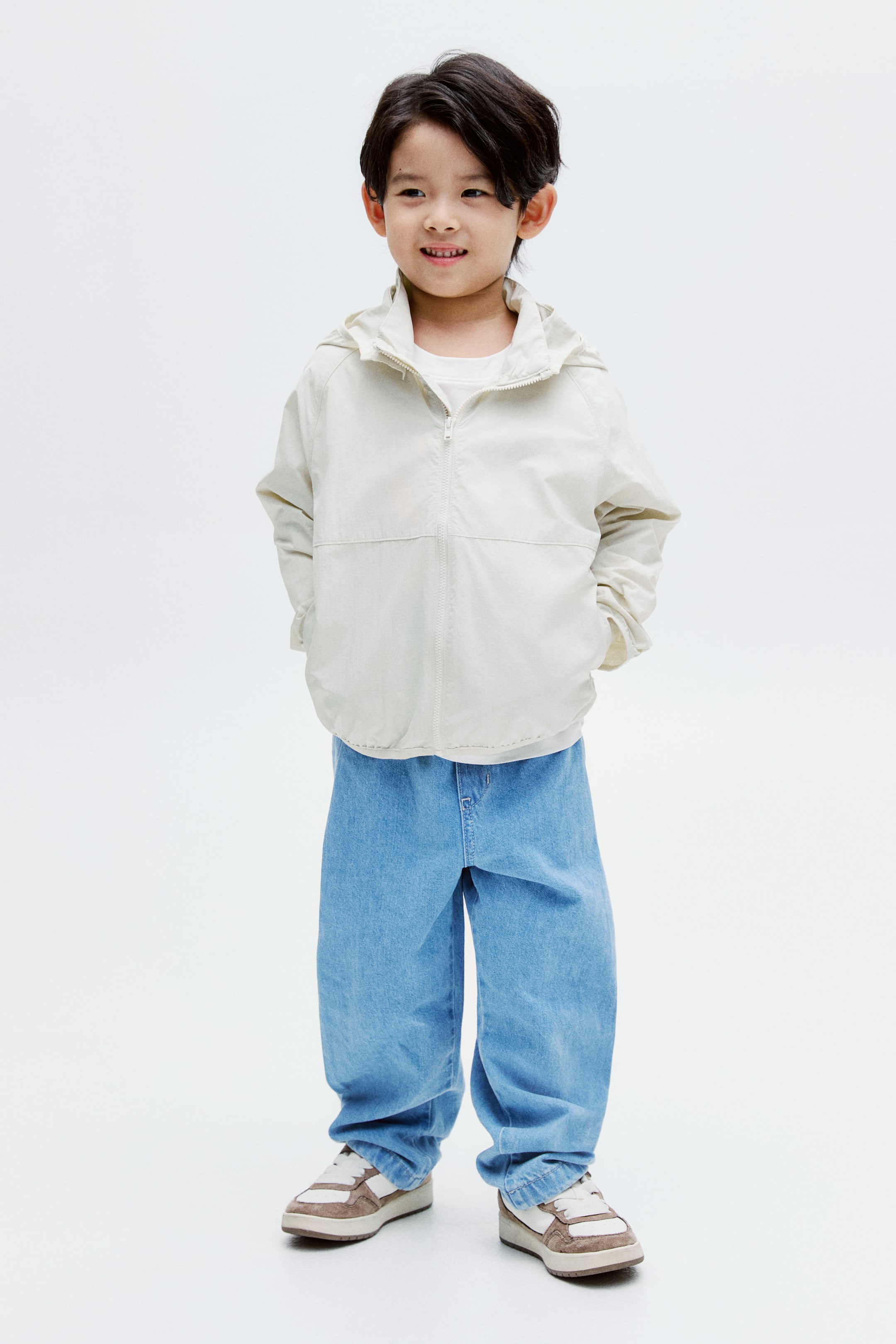 View larger image: A light beige hooded jacket is being presented from the front, slightly angled to the right. It is featuring a full zipper closure down the center and an attached hood. The jacket is showcasing long sleeves and visible side pockets, and it is being worn over a white t-shirt.