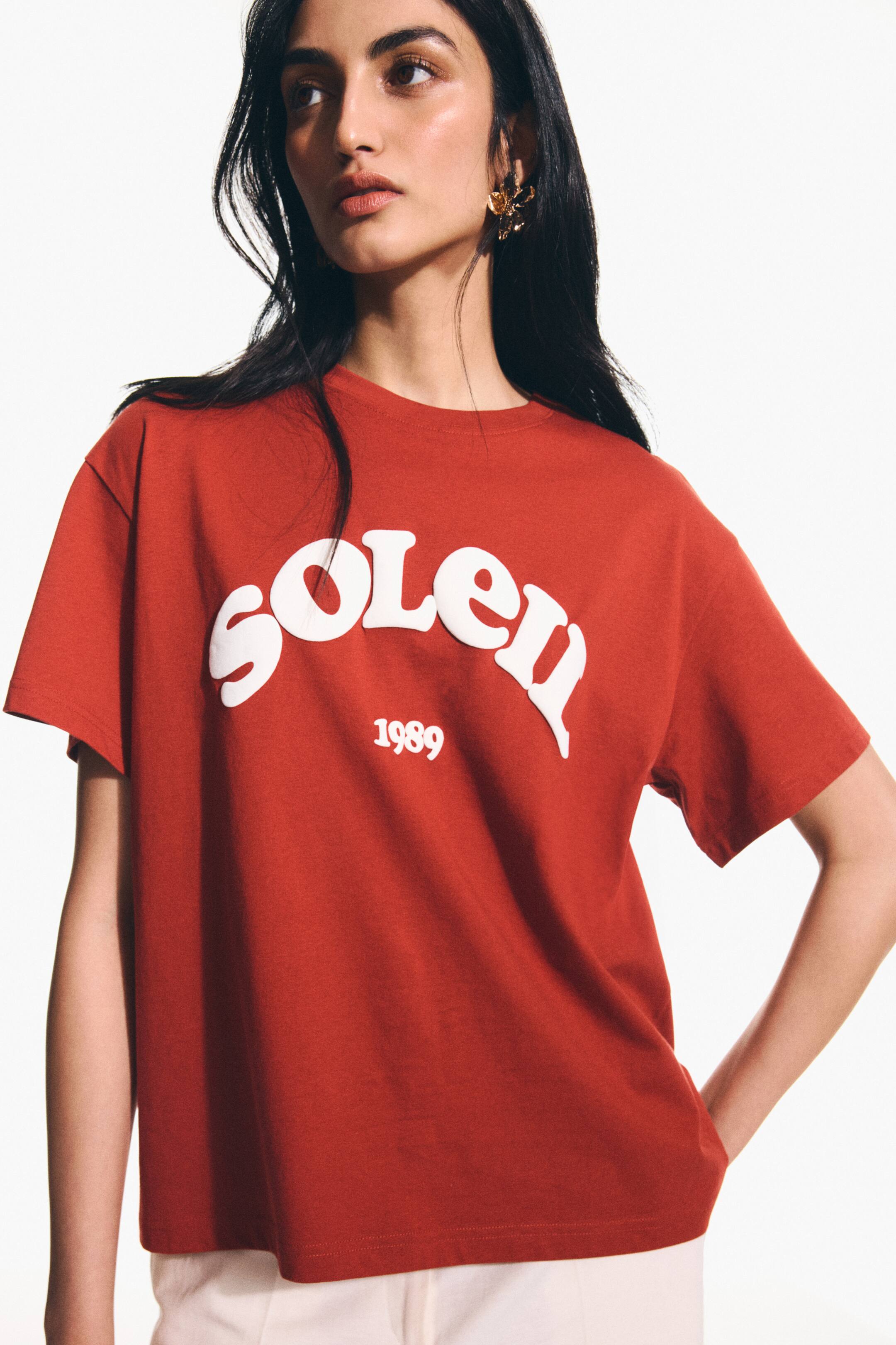 View larger image: A red crew neck t-shirt showcasing a raised, arched white "SOLEN" graphic with "1989" beneath on the chest. It features short sleeves and a relaxed fit, displayed from a slightly angled front view.