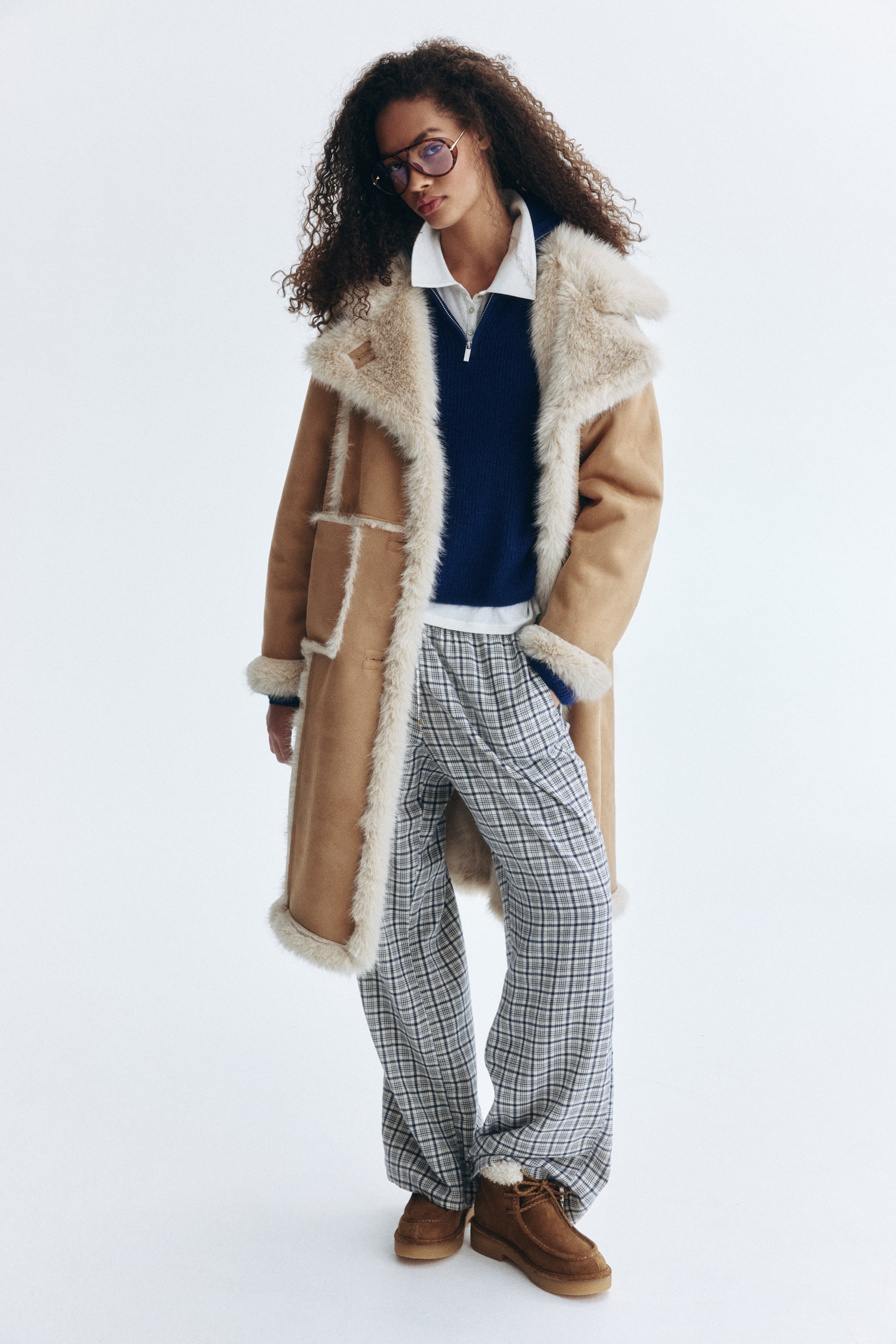 Agrandir l'image: Un manteau droit dans un tissu tissé beige avec une finition douce et duveteuse est porté par le mannequin. Il présente des garnitures pelucheuses de couleur claire, un col et une doublure, ainsi que des revers crantés, des boutons sur le devant et des poches plaquées sur le devant. Le mannequin met une main dans une poche.