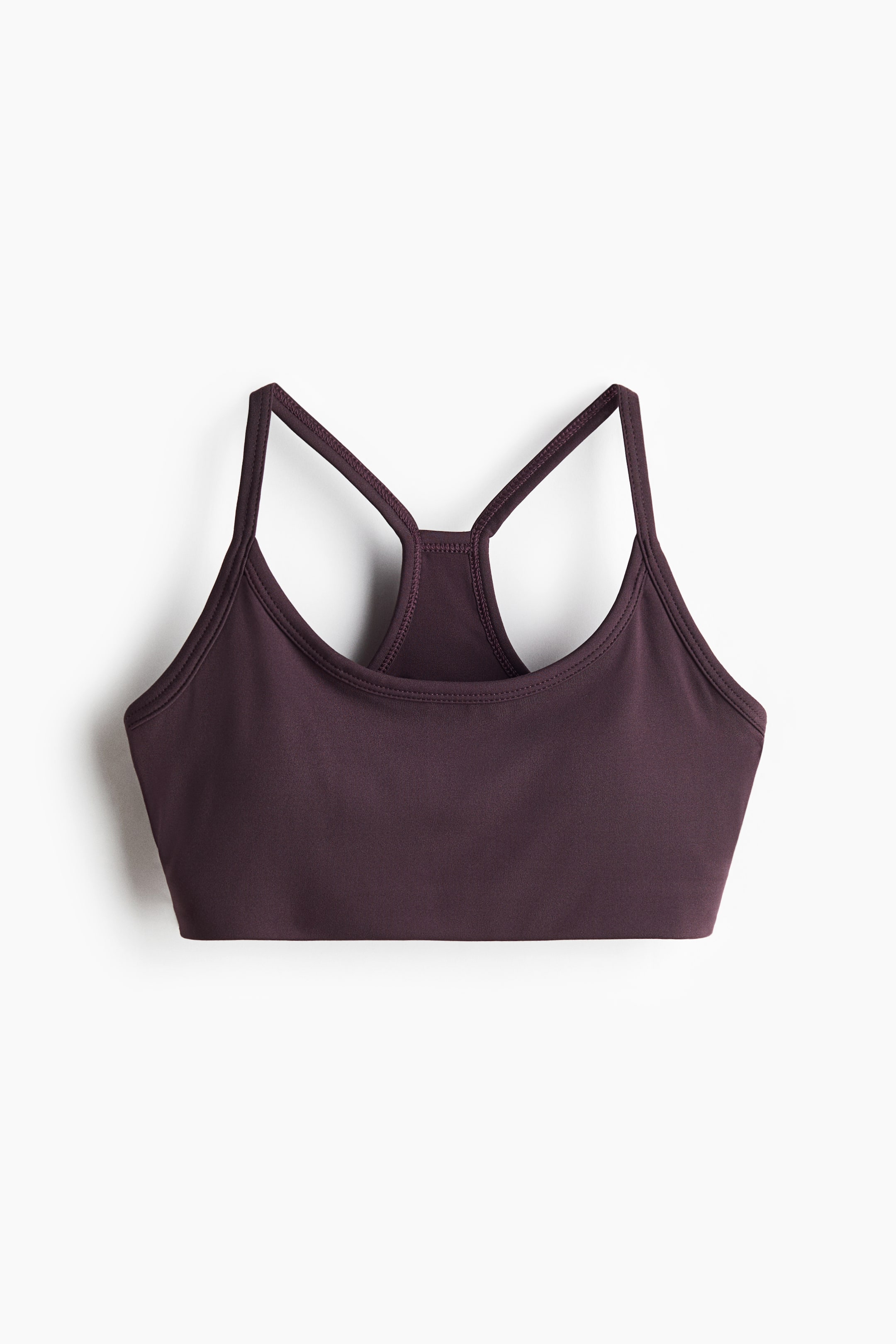 Visa större bild: Den lätt vadderade sport-bh:n i crop top-modell visas framifrån och har en mörk plommonfärg, en rundad halsringning och tunna racerback-band.