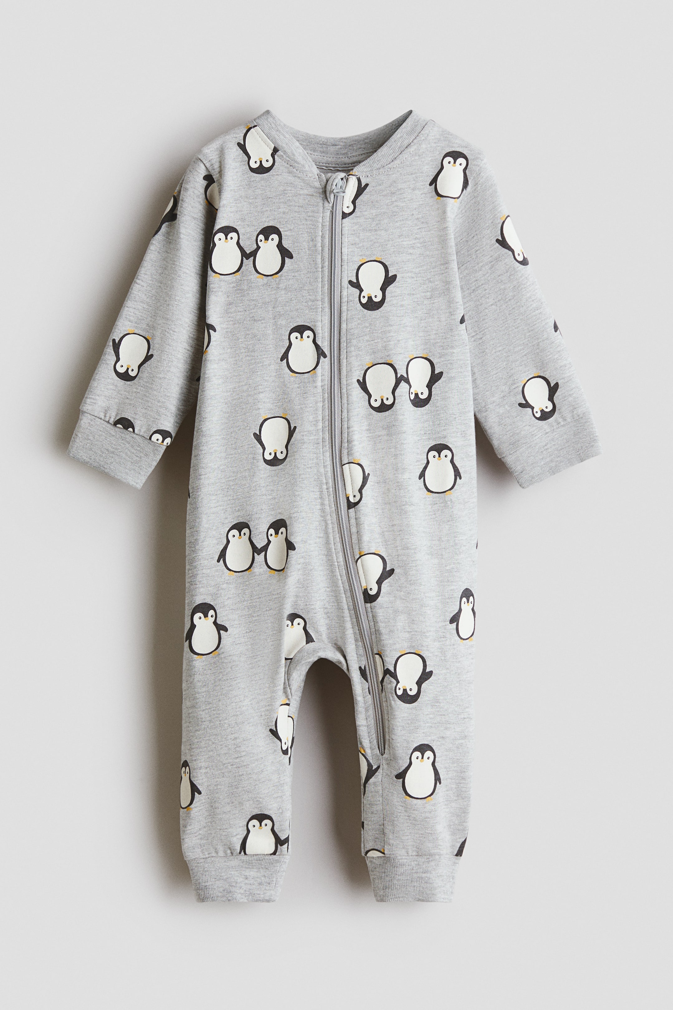 View larger image: A long-sleeved sleepsuit in soft grey cotton jersey features an all-over penguin print, shown from the front. A zip runs down the front and along one leg, with an anti-chafe chin guard at the top, while ribbed cuffs and hems complete the garment.