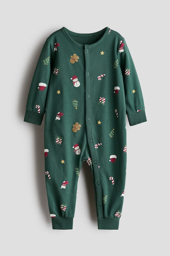 En grÃ¸nn sleepsuit i bomullsjersey vises forfra med et gjennomgÃ¥ende festlig trykk av snÃ¸menn, pepperkakemenn, polkagrisstenger og juletre. Den har lange ermer med ribbestrikkede mansjetter, lange ben med ribbestrikkede kanter og en trykknappelukking som gÃ¥r ned midt foran og langs det ene benet. - 1