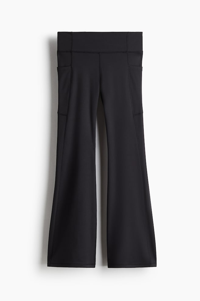 A pair of black flared leggings is shown from the FRONT, featuring a wide, high-rise waistband. The leggings are designed with two side slip pockets on the thighs and are flaring from the knee down to the hem. - 1