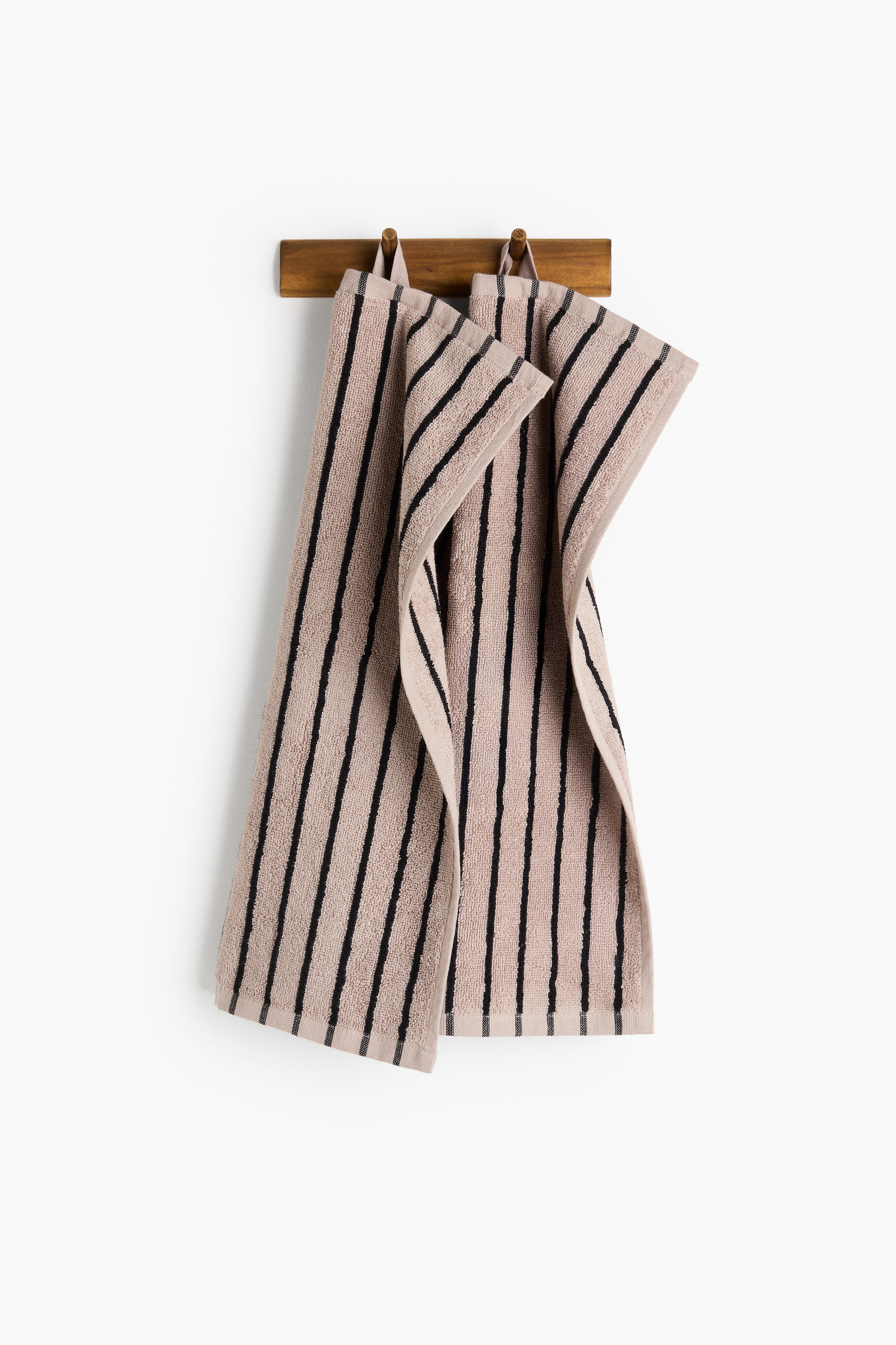 View larger image: A pair of guest towels is hanging, showcasing a soft terry texture in beige with black vertical stripes. Each towel features a woven hem and a loop on one short side for hanging.