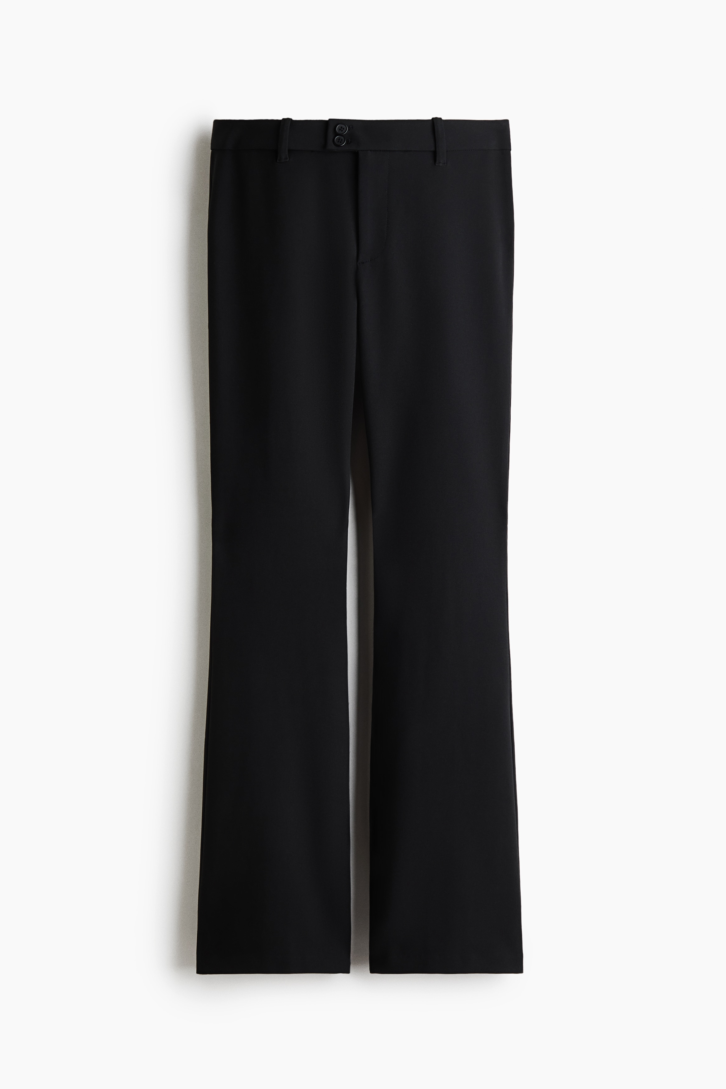 Black fitted trousers in a stretch weave, featuring an extended waistband with two buttons and a bootcut silhouette, are worn by the model. The trousers are styled with a black halter top, an open black faux fur jacket, and black flat shoes.
