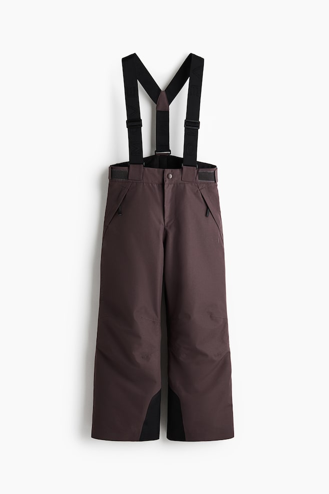 Ein Paar dunkelbraune Schneehosen ist von vorne zu sehen und verfÃ¼gt Ã¼ber verstellbare schwarze elastische HosentrÃ¤ger mit Y-RÃ¼cken-Design. Die Hose zeigt einen Bund mit Druckknopfverschluss und verstellbaren Seitenschnallen, Handtaschen mit ReiÃverschluss, vorgeformte Knie und verstÃ¤rkte schwarze InnenbeinabschlÃ¼sse. - 1