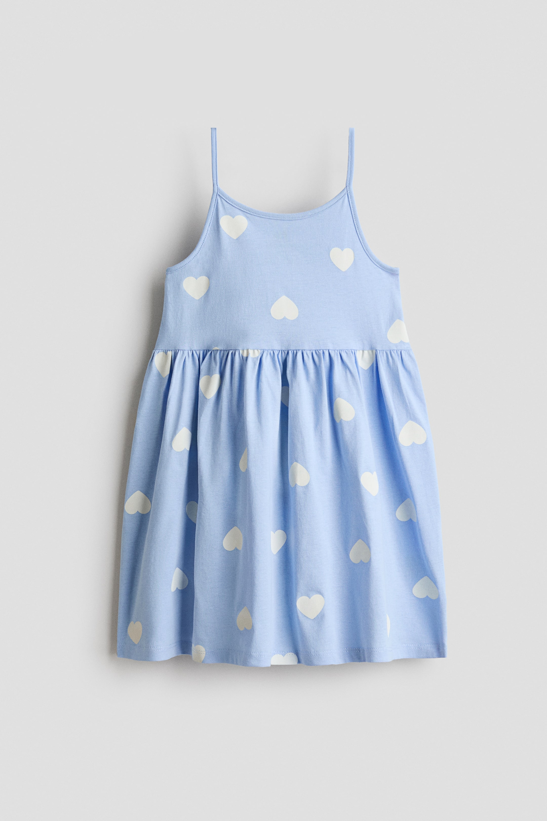 이미지 확대 보기: 부드러운 코튼 저지 소재의 연한 파란색 드레스가 앞면을 보여주고 있으며, 좁은 어깨 끈과 전체적으로 흰색 하트 패턴이 특징입니다. 허리 부분에는 주름이 잡혀 있고, 부드럽게 퍼지는 스커트로 디자인되었습니다.