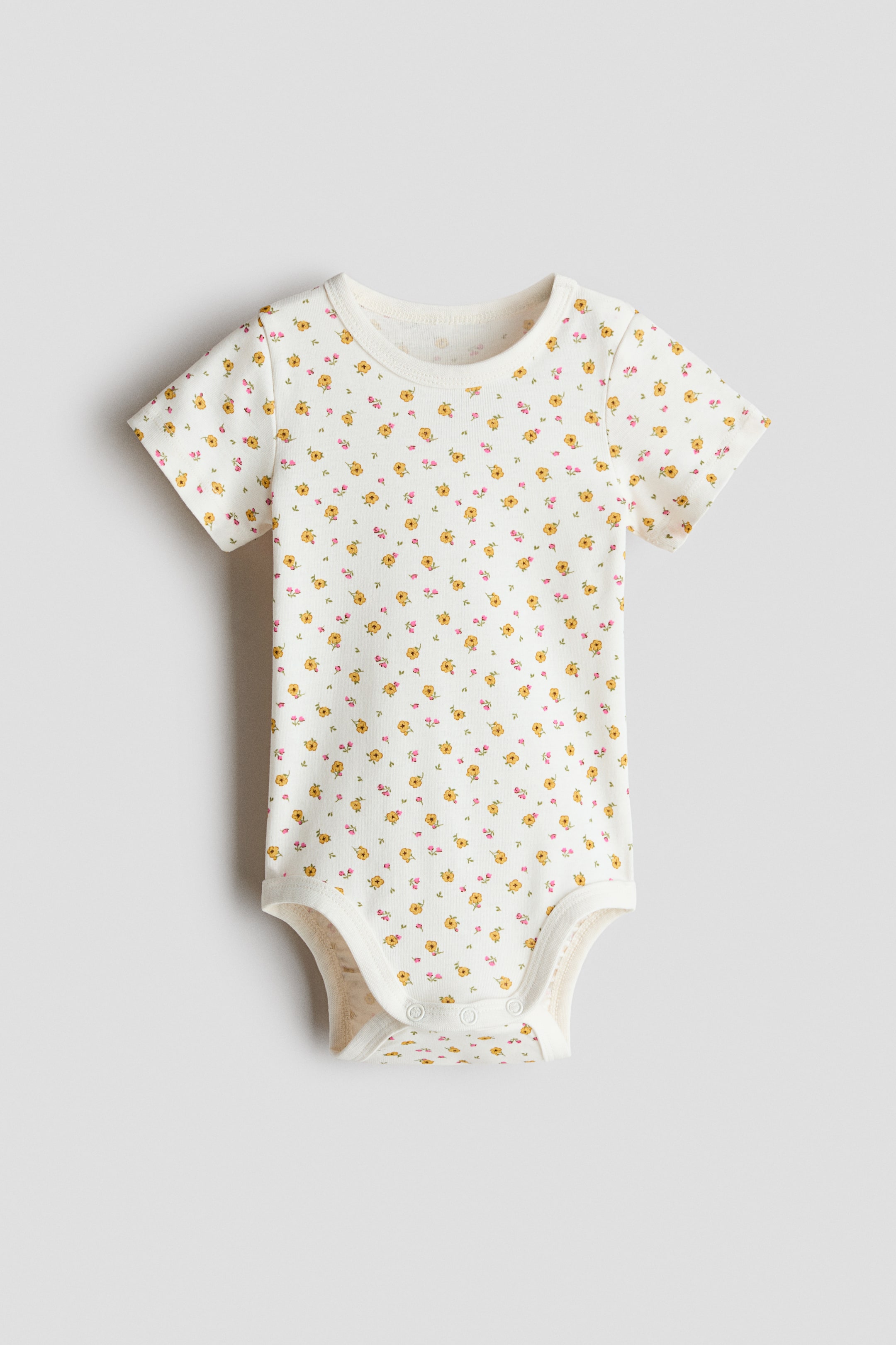 View larger image: A short-sleeved bodysuit crafted from cream soft cotton jersey fabric, adorned with an all-over print of petite yellow and pink flowers. It boasts a round, trimmed neckline, short sleeves, and press-studs on one shoulder and at the bottom.
