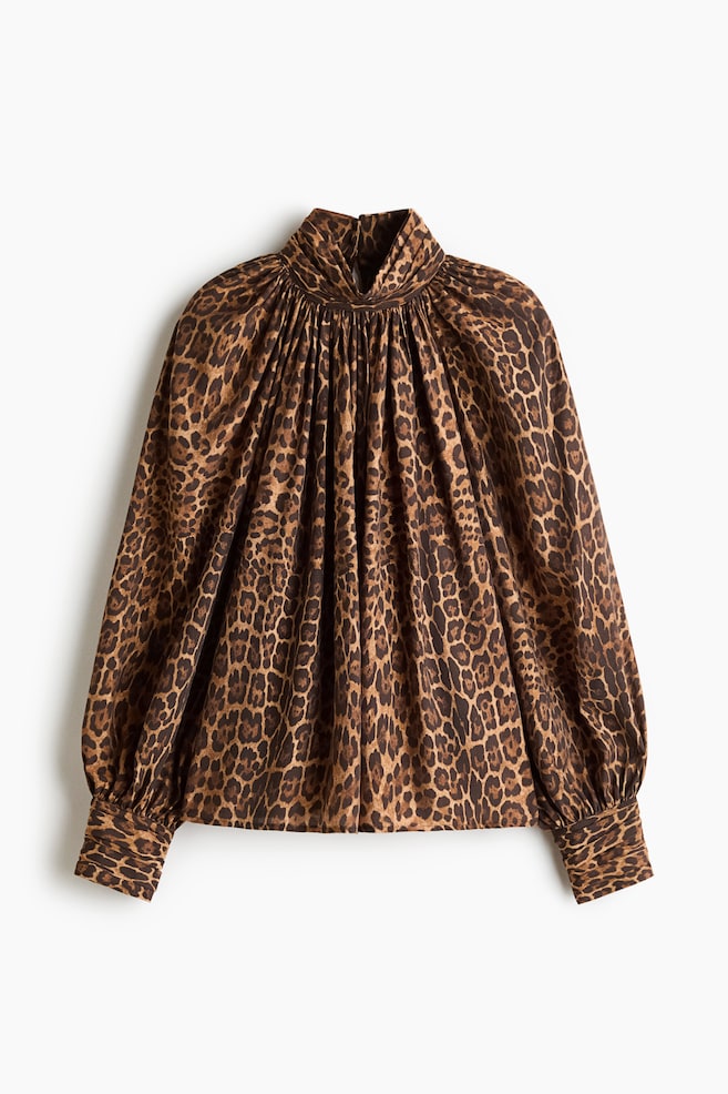En blus med leopardmönster i brunt och svart har en rynkad hög halsringning, en ledig passform och långa, voluminösa ärmar med vida manschetter. - 1