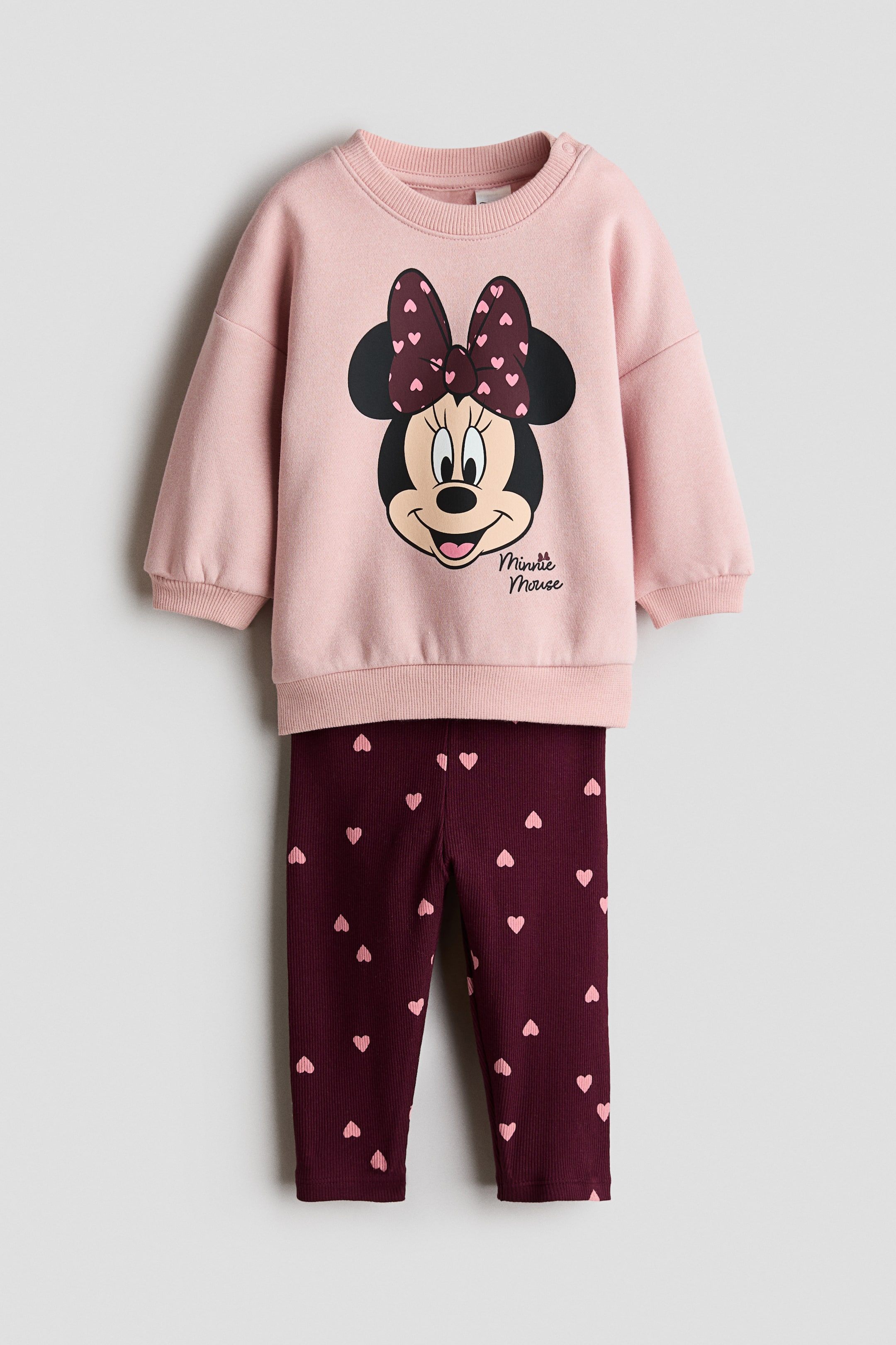 View larger image: A 2-piece printed set features a pink long-sleeved sweatshirt with a front Minnie Mouse face print, complete with a polka-dot bow and ribbed cuffs and hem. Burgundy ribbed leggings complete the set, with an all-over pink heart print.