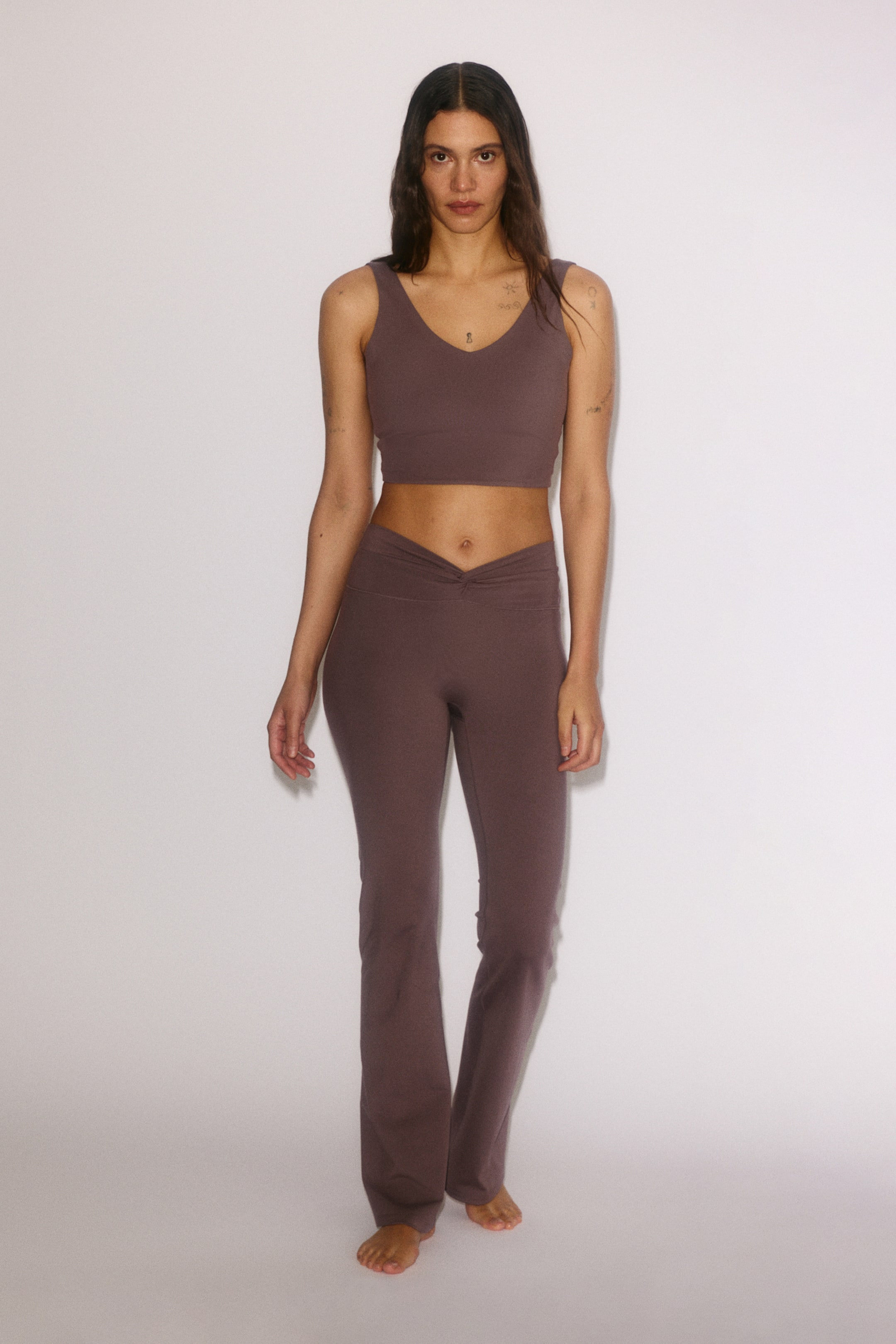 View larger image: A matching two-piece set in a muted purple-brown is showcased from the front. It features a ribbed V-neck crop top and coordinating ribbed pants with a V-shaped crossover waistband and flared legs.