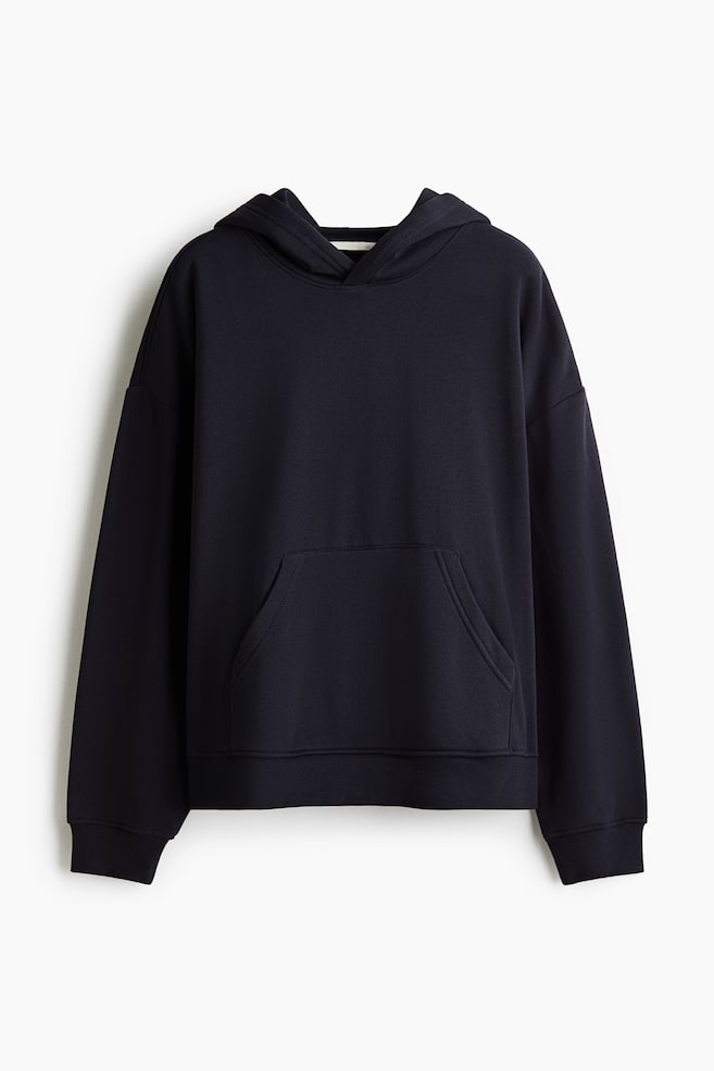 A dark navy blue hoodie is hanging front-facing, featuring a double-layer hood, low dropped shoulders, and a front kangaroo pocket. The long sleeves end in ribbed cuffs, and the bottom hem is finished with matching ribbing. - 1