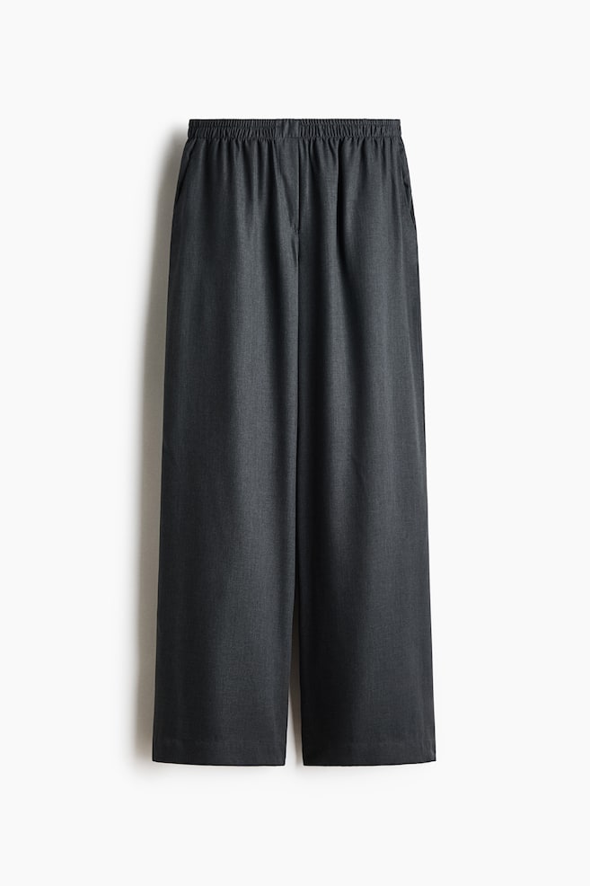 Estos pantalones de pierna ancha en gris oscuro se muestran de frente, con una cintura elÃ¡stica fruncida y discretos bolsillos laterales. El diseÃ±o ofrece un corte holgado y relajado, con perneras rectas y amplias en un tejido texturizado de color carbÃ³n. - 1