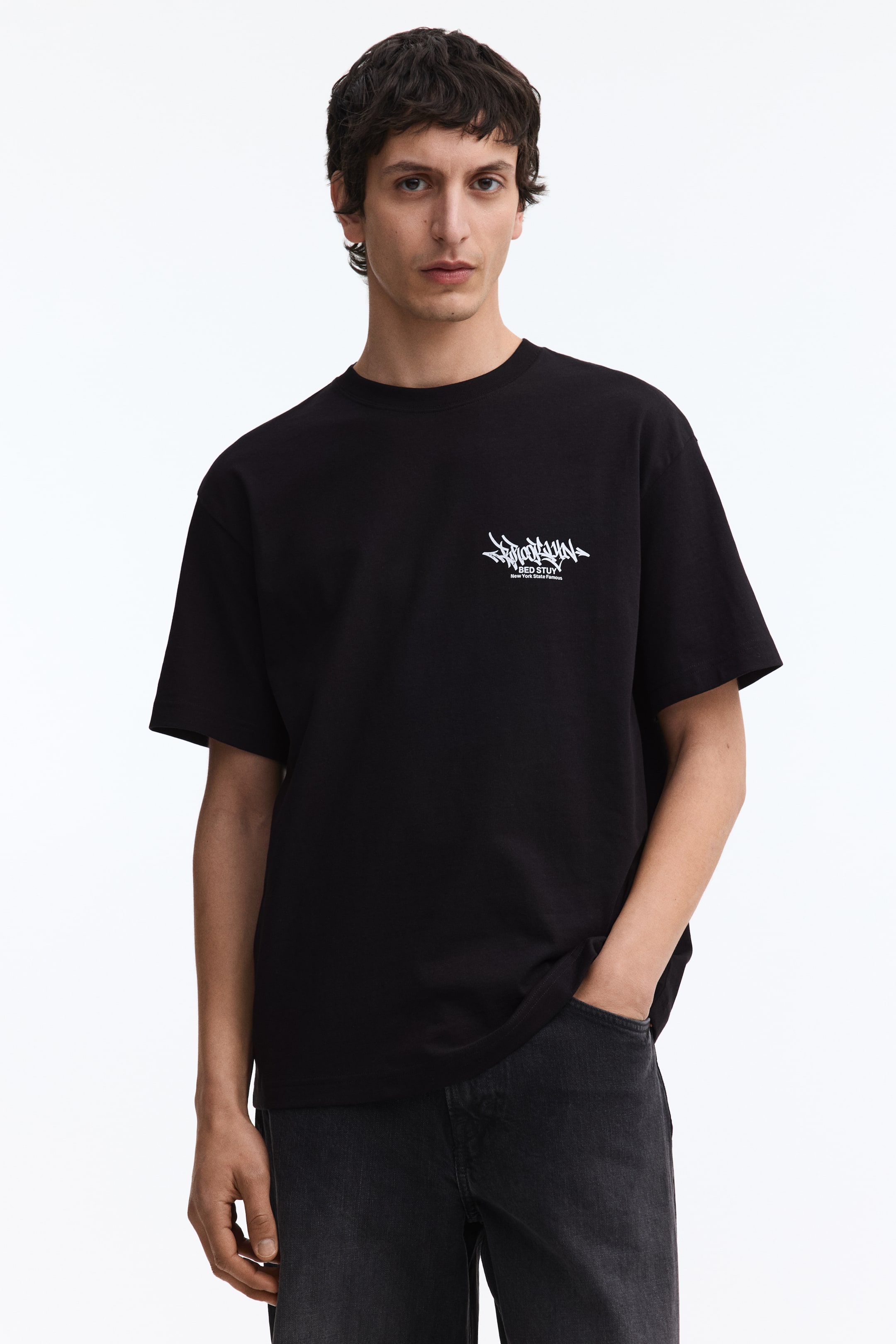 View larger image: A black short-sleeve t-shirt features a white graphic print on the left chest, showcasing stylized text "BROOKLYN" above "BED STUY" and "New York State Famous."