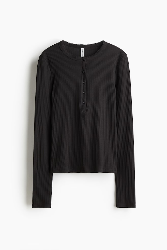 Se muestra una camiseta negra de manga larga acanalada desde el frente, con un escote redondo adornado con un ribete festoneado y una tapeta Henley de cinco botones. - 1