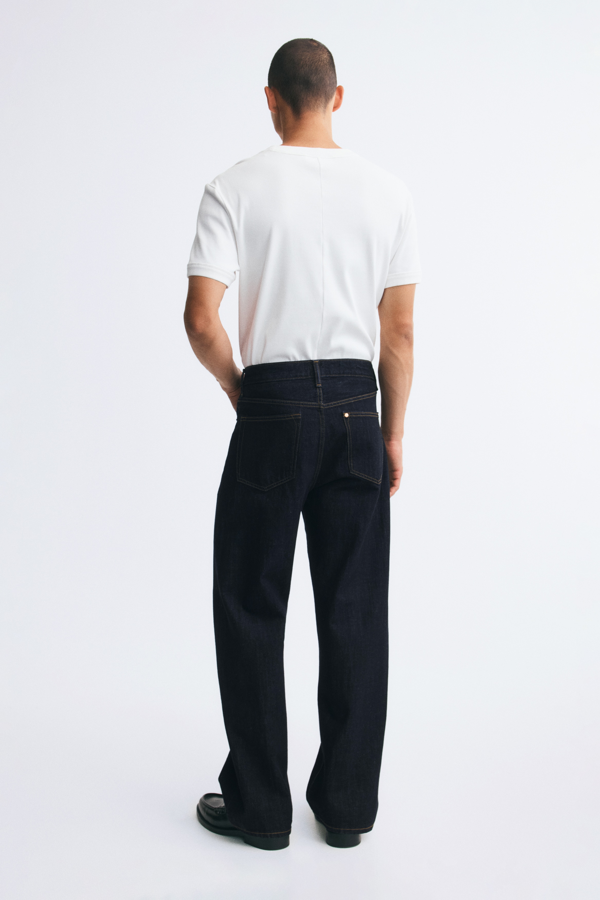 Dark blue jeans are laid flat, facing forward, featuring a straight-leg cut with contrasting orange stitching. They showcase two front pockets with copper-toned rivets, a coin pocket, and a visible silver-toned button closure at the waist.