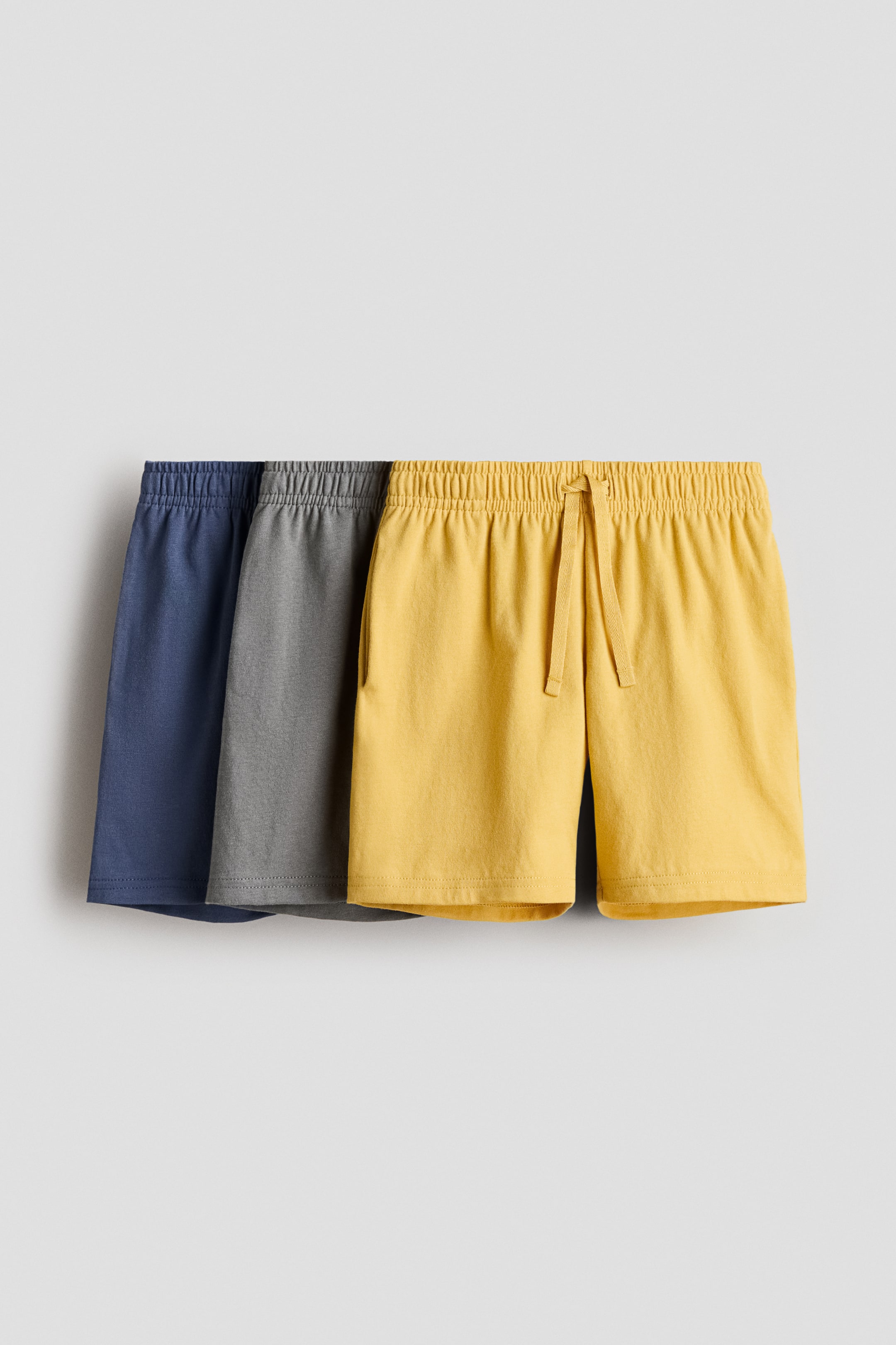 View larger image: Knee-length shorts in soft cotton jersey are shown from the front, presented in a set of three: blue, gray, and yellow. Each pair features an elasticated, drawstring waist and discreet side seam pockets.