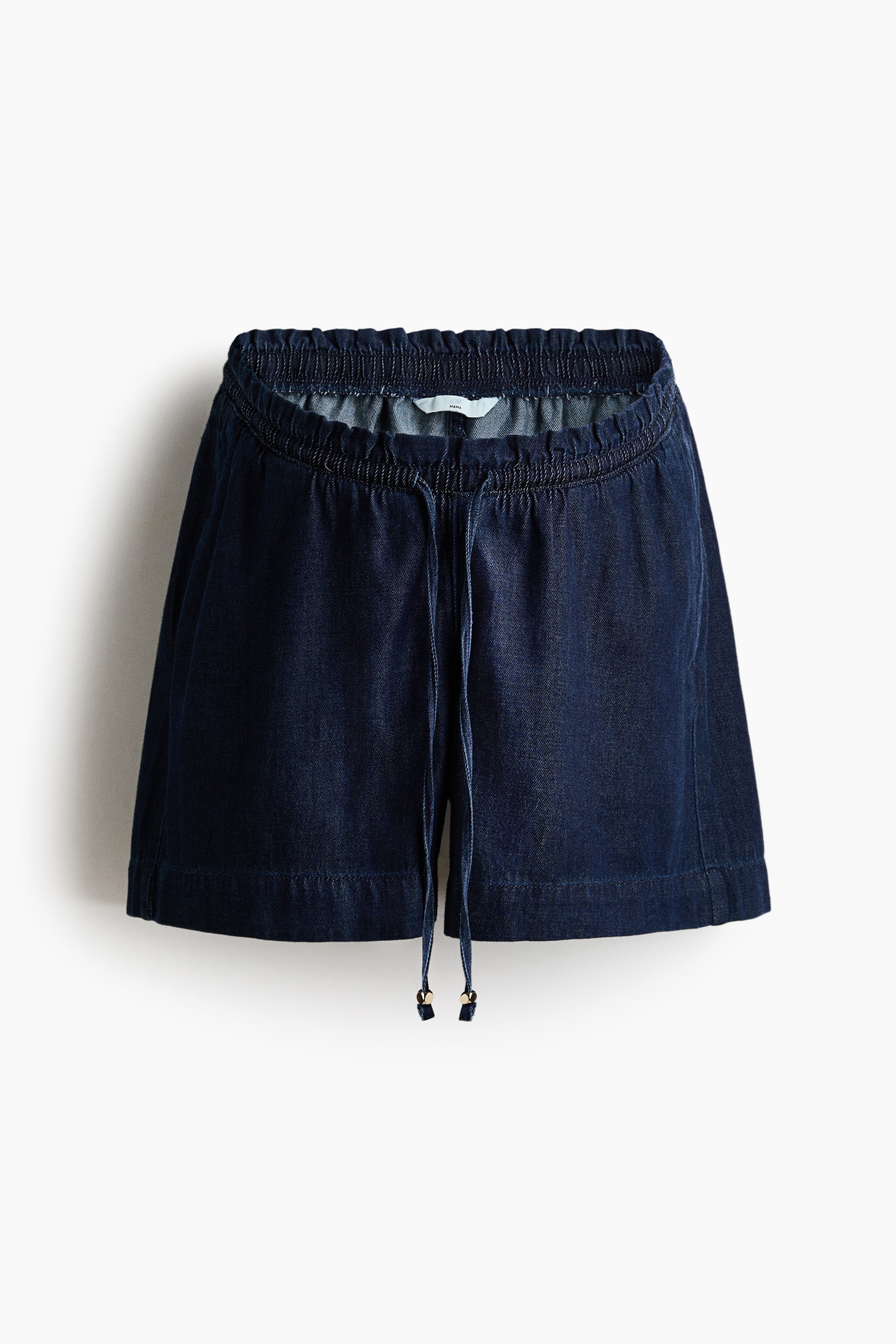 Agrandir l'image: Vue de face d'un short en denim bleu foncé. Une taille élastiquée et plissée est visible en haut, accompagnée d'un cordon de serrage terminé par des embouts en métal doré. Le short présente une coupe large et décontractée.