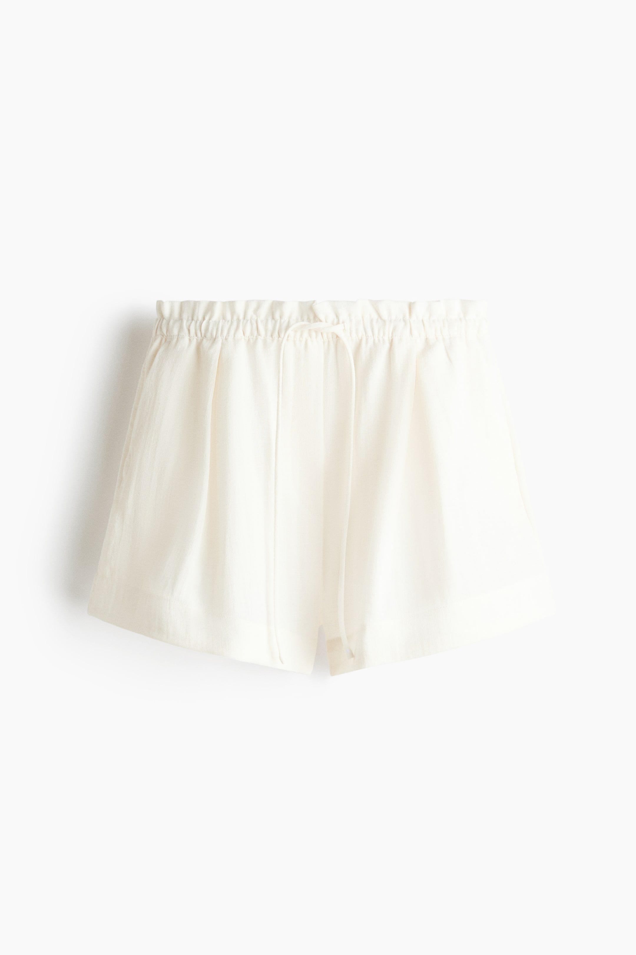 View larger image: The cream-coloured shorts boast an elasticated, gathered waistband with a drawstring tie at the front. The loose-fitting shorts feature small side slits at the hem.