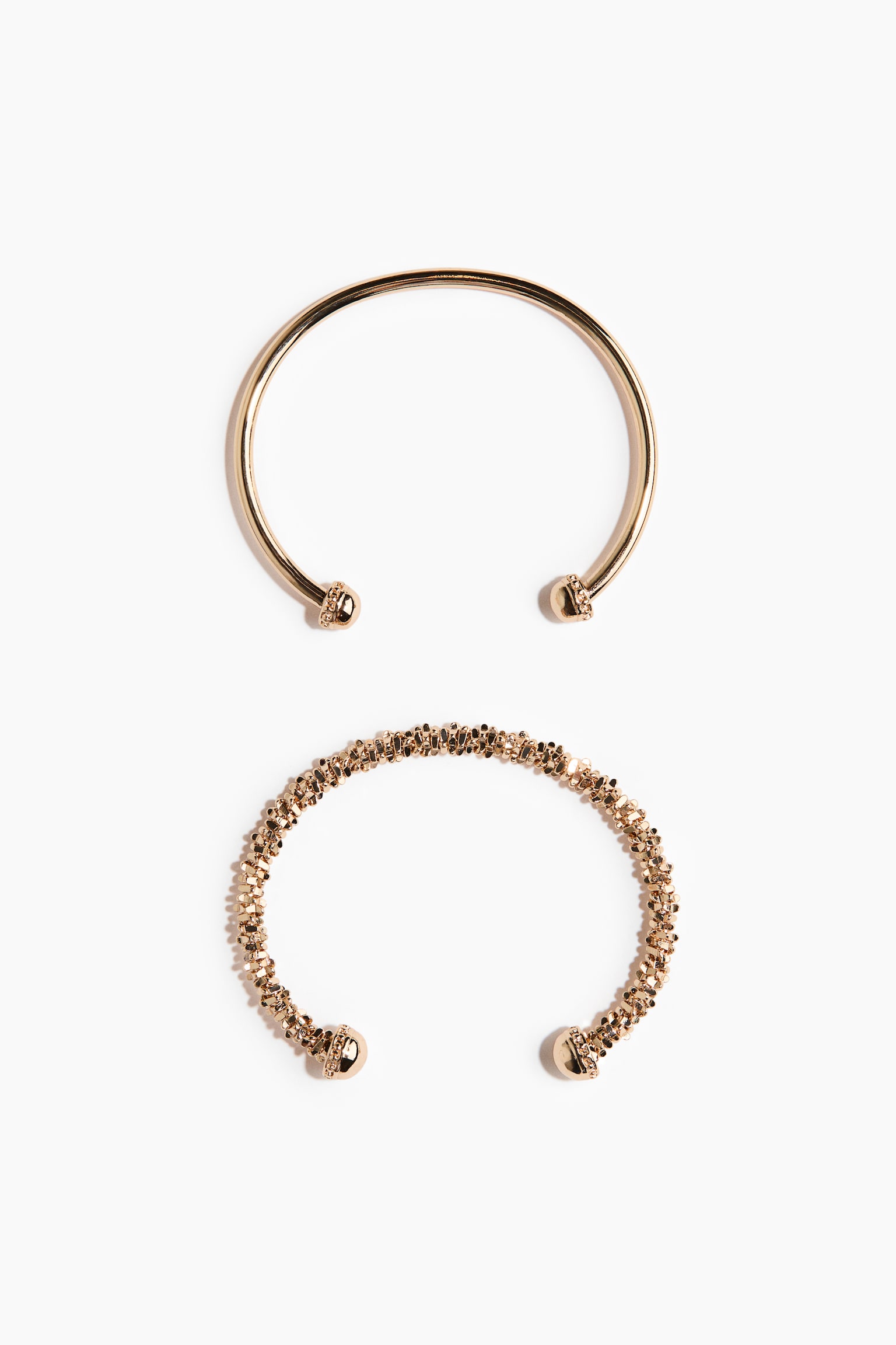 Dua gelang terbuka berwarna emas ditunjukkan dari pandangan atas. Gelang atas menampilkan jalur licin dengan hujung sfera kecil yang bertekstur, manakala gelang bawah mempamerkan jalur bertekstur granular dengan hujung sfera yang lebih besar dan bertekstur. - 1