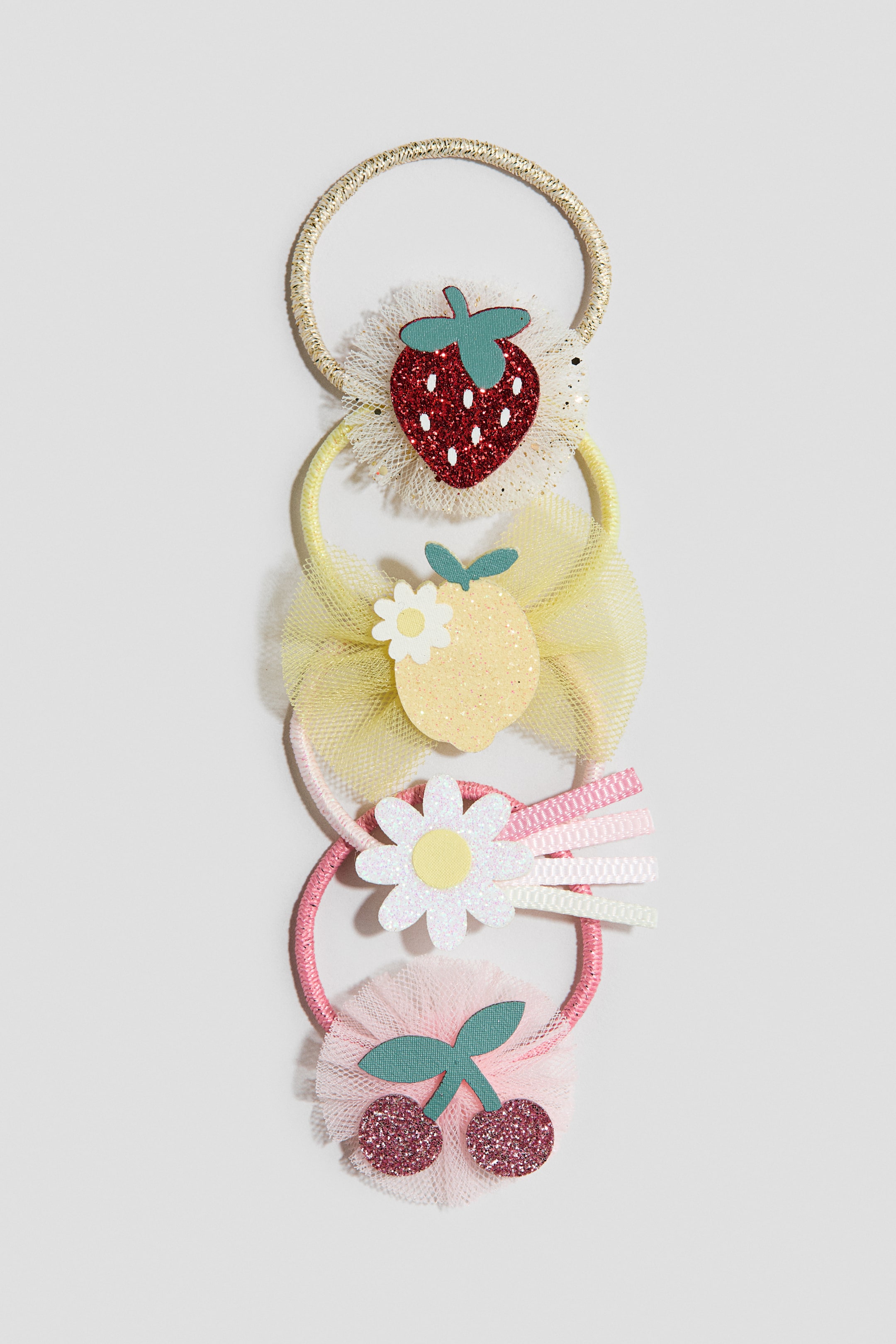 הצגת תמונה גדולה יותר: סט של ארבע גומיות שיער מוצג בצורה אנכית, כל אחת פונה קדימה ומציגה אלמנט דקורטיבי ייחודי המחובר לגומייה צבעונית. הגומיות מציגות תות מנצנץ אדום על רפול טול בצבע קרם עם רצועת זהב, לימון מנצנץ צהוב עם פרח לבן קטן על קשת טול צהובה עם רצועה צהובה, חיננית מנצנצת לבנה עם רצועות סרט ורוד ולבן על רצועה ורודה, ושתי דובדבנים מנצנצים ורודים כהים על רפול טול ורוד עם רצועה ורודה.