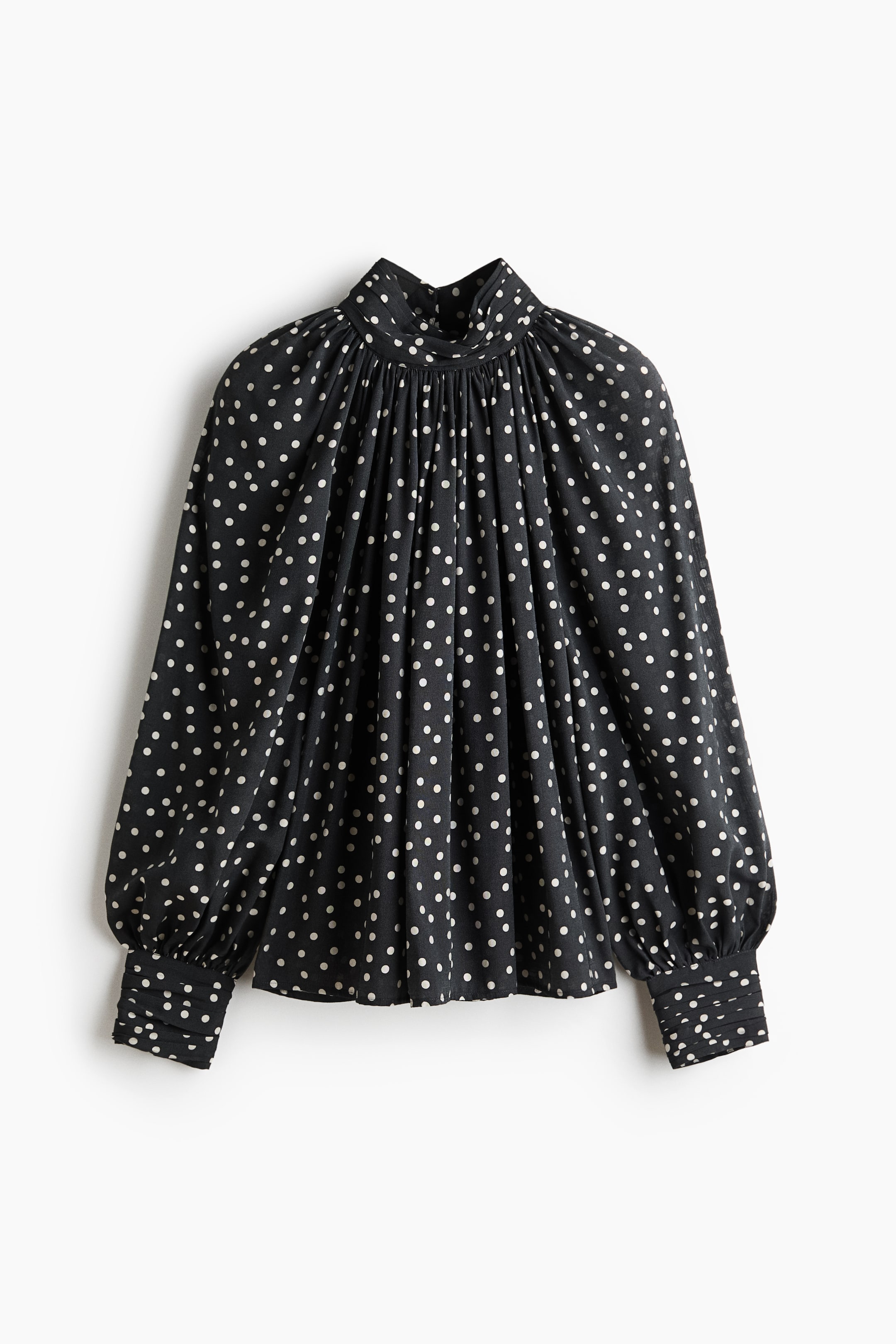 View larger image: A black blouse with white polka dots is showcasing a gathered mock neck, long voluminous sleeves, and shirred cuffs.