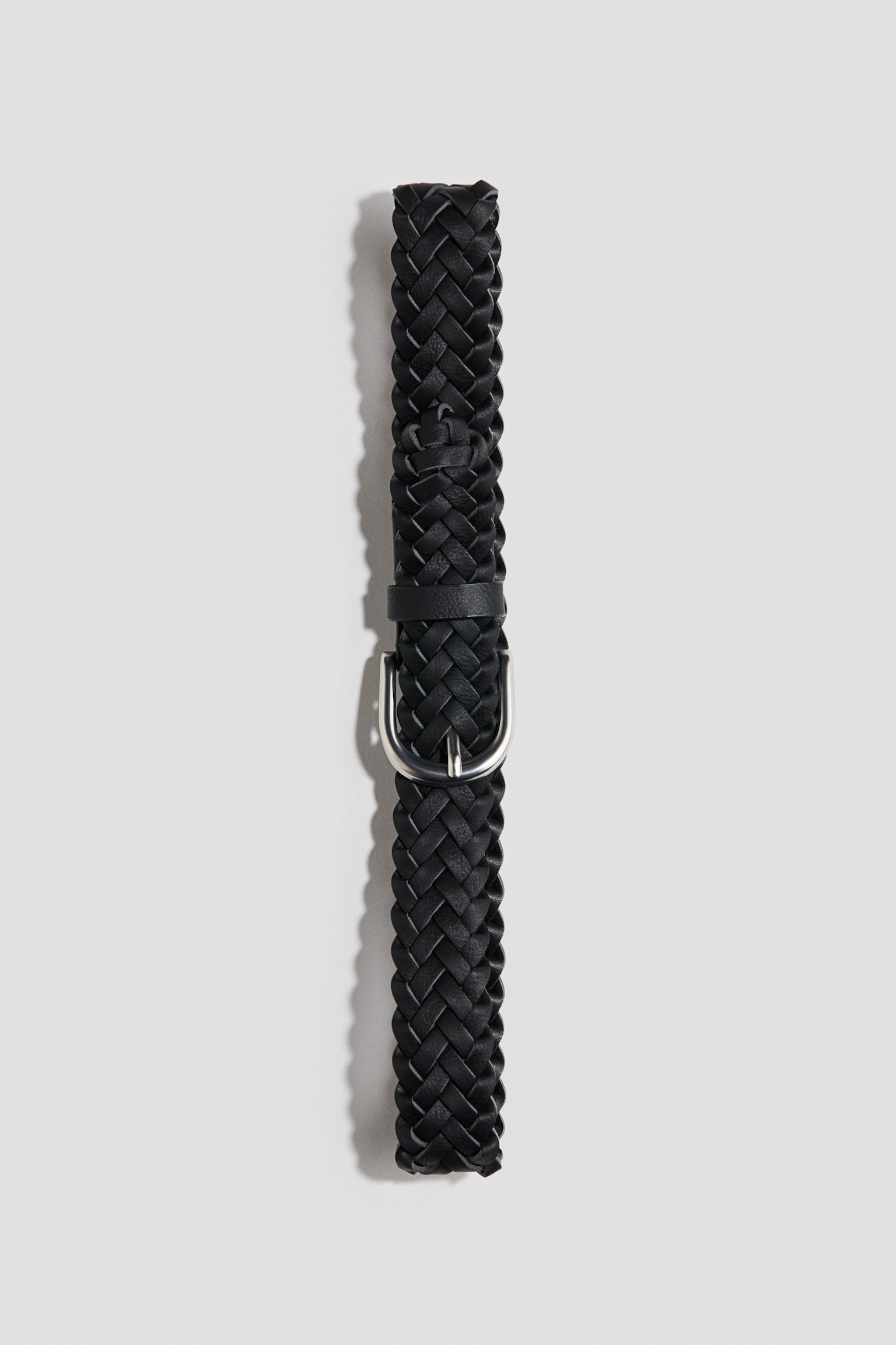 A black braided belt is lying vertically, facing forwards to showcase its design. It features a tightly woven strap, a matching leather keeper loop, and a rounded silver-tone metal buckle.