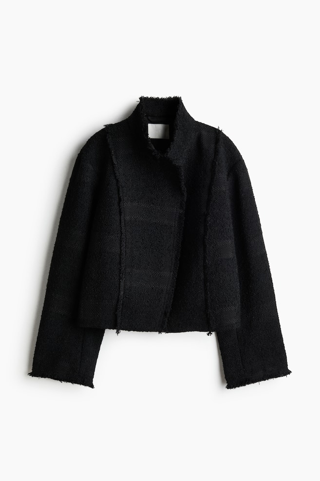 Une veste courte noire prÃ©sente un tissu texturÃ© de type bouclÃ© et un design de face avec un col montant haut. Elle se distingue par un croisÃ© asymÃ©trique sur le devant, de larges manches longues, ainsi que des bords bruts et effilochÃ©s le long des coutures, du col, des poignets et de lâourlet. - 1
