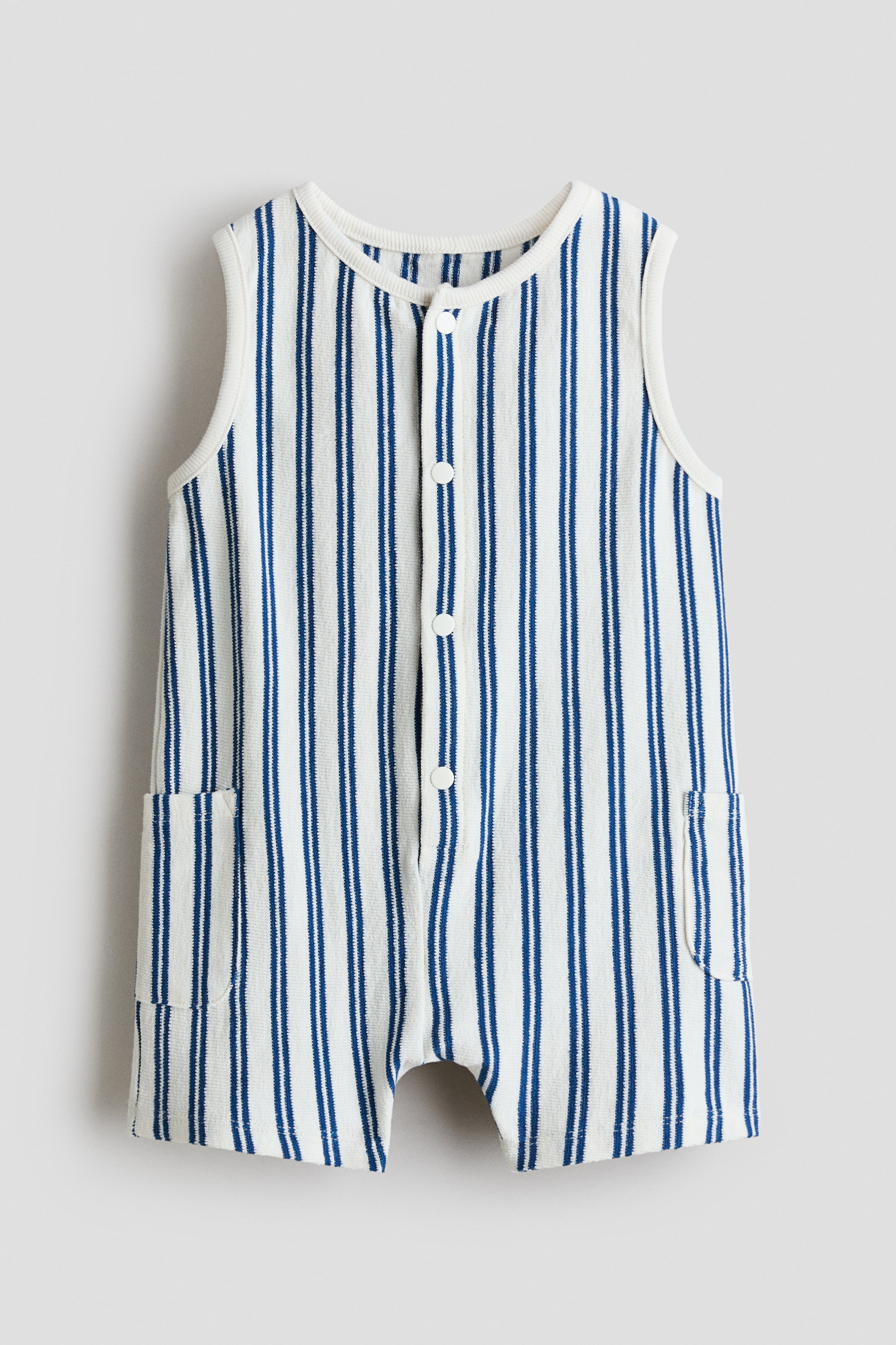 View larger image: The baby romper is showcased from the front, highlighting white and blue vertical stripes on a terry knit fabric. It features a round ribbed neckline, ribbed sleeveless armholes, a full-length front button placket with white buttons, and two front patch pockets.