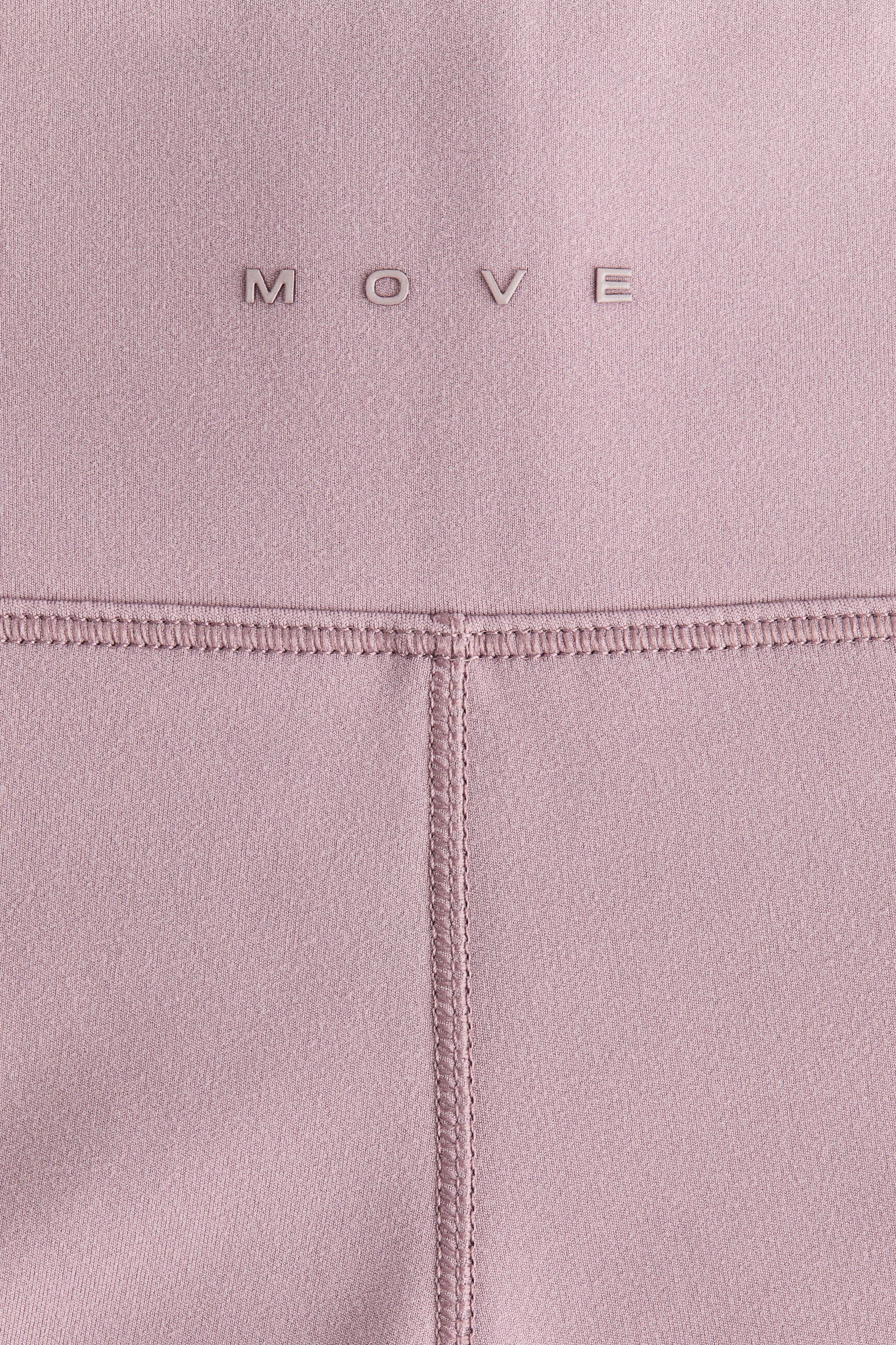 Προβολή μεγαλύτερης εικόνας: Αθλητικά κολάν με επένδυση από fleece και τεχνολογία SoftMove? διαθέτουν ένα απαλό ροζ ύφασμα, στο οποίο αναγράφεται η λέξη 'MOVE' με μεταλλική γραμματοσειρά στο πάνω μέρος. Υπάρχει μια οριζόντια ραφή flatlock που διατρέχει το πάνω μέρος, από την οποία επεκτείνεται μια κάθετη ραφή flatlock προς τα κάτω.