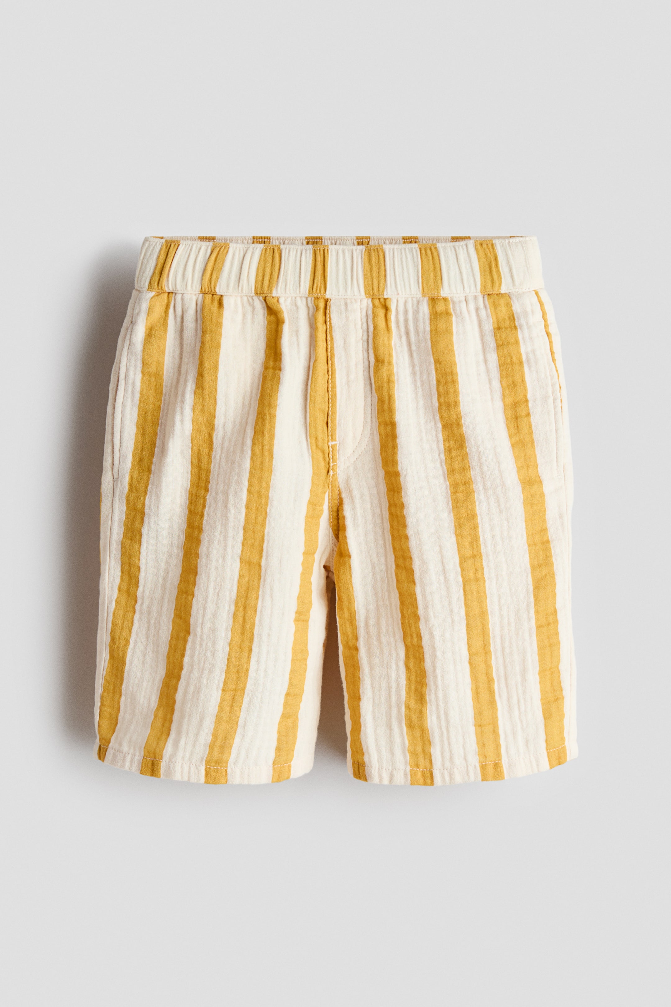 View larger image: The shorts showcase a FRONT design, adorned with vertical mustard yellow and cream stripes on a textured, crinkled fabric, extending just above the knee. Crafted with an elasticated waistband and side pockets, they offer both style and comfort.