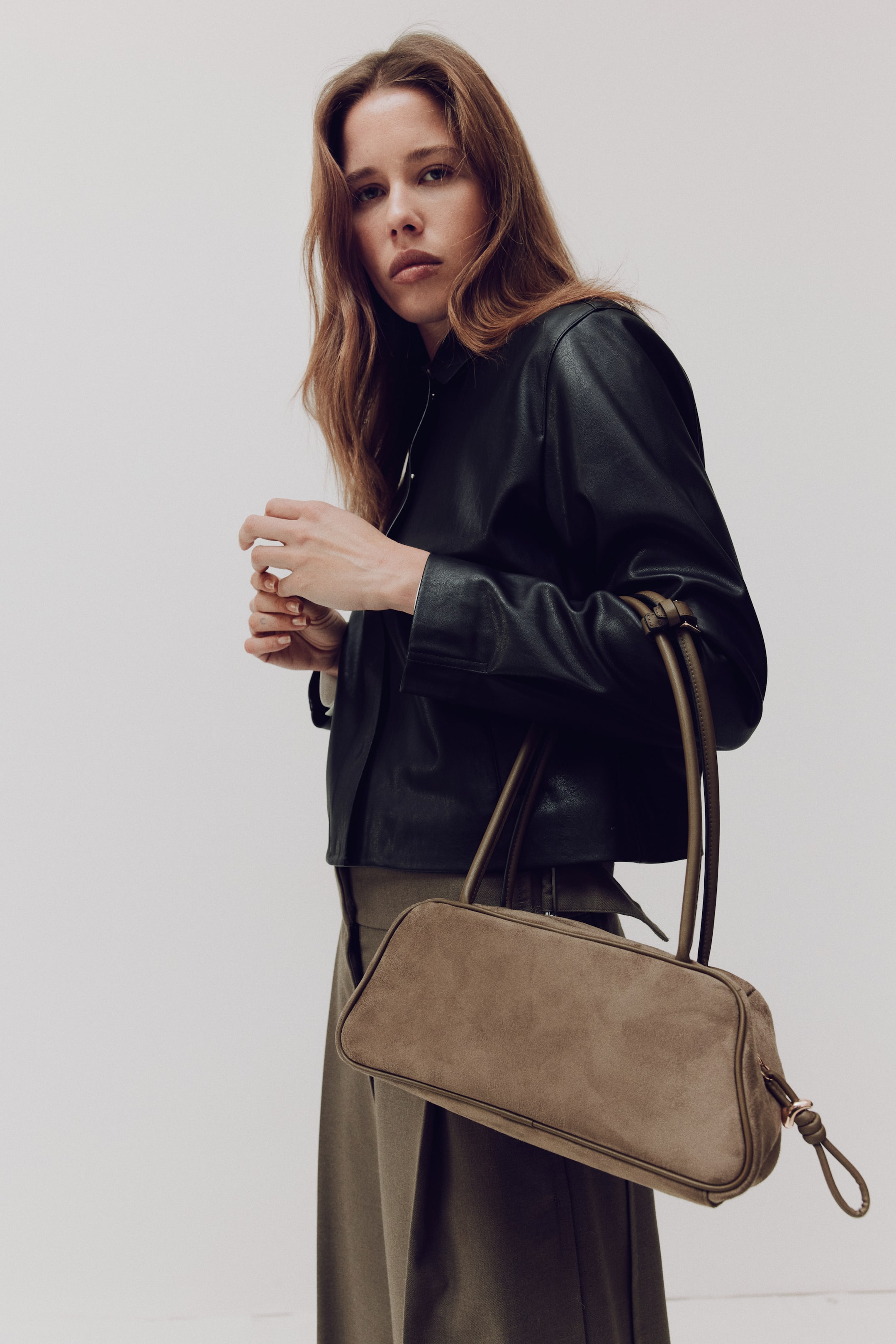 View larger image: A shoulder bag with a soft, napped finish and coated-fabric detailing, angled to the right. It features a zip closure at the top with a knotted pull tab, and long handles secured together with a tab and metal buckle.