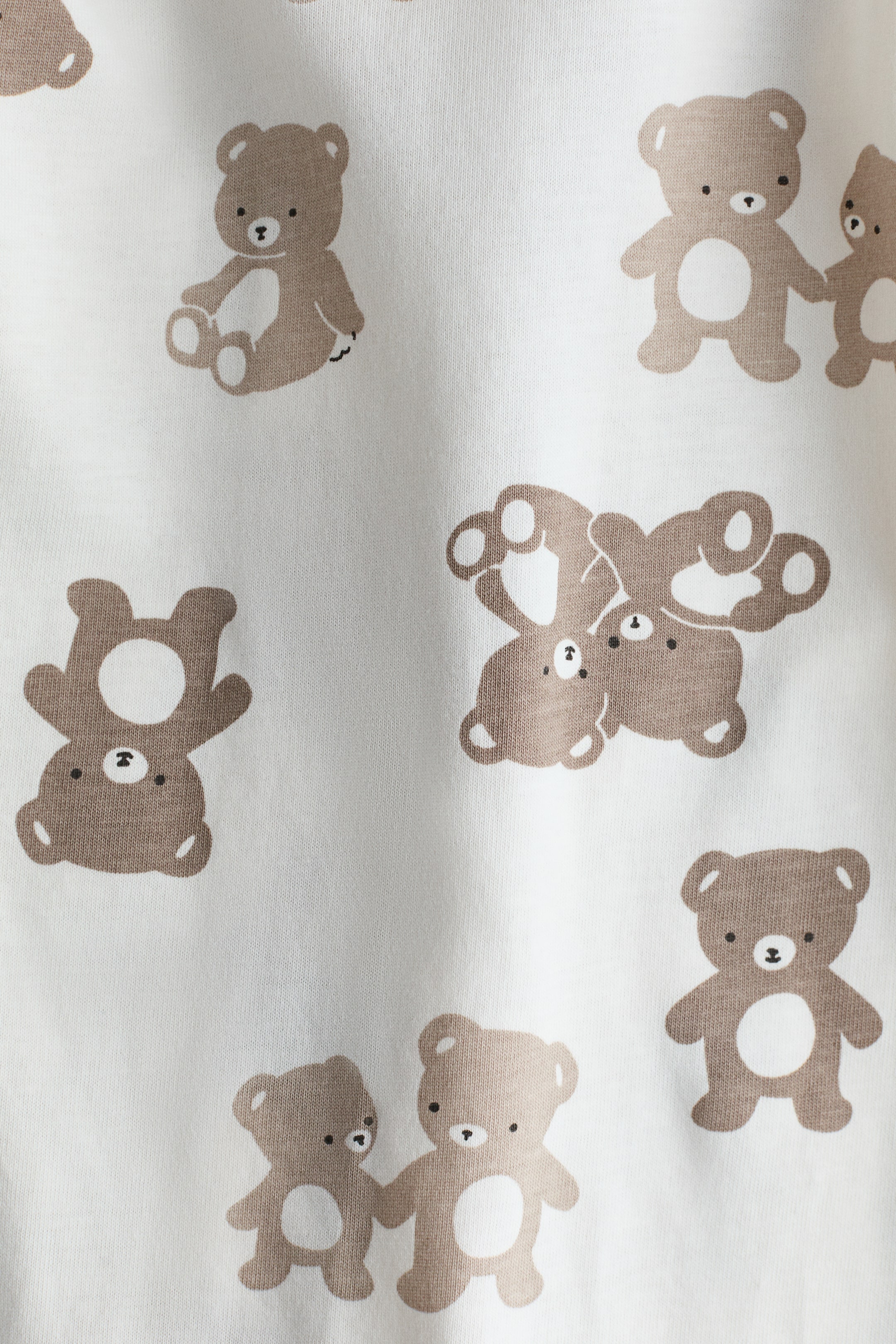 Grotere afbeelding bekijken: De witte katoenen jersey-stof van het slaapzakje is bedrukt met een all-over print van bruine teddyberen in verschillende houdingen.