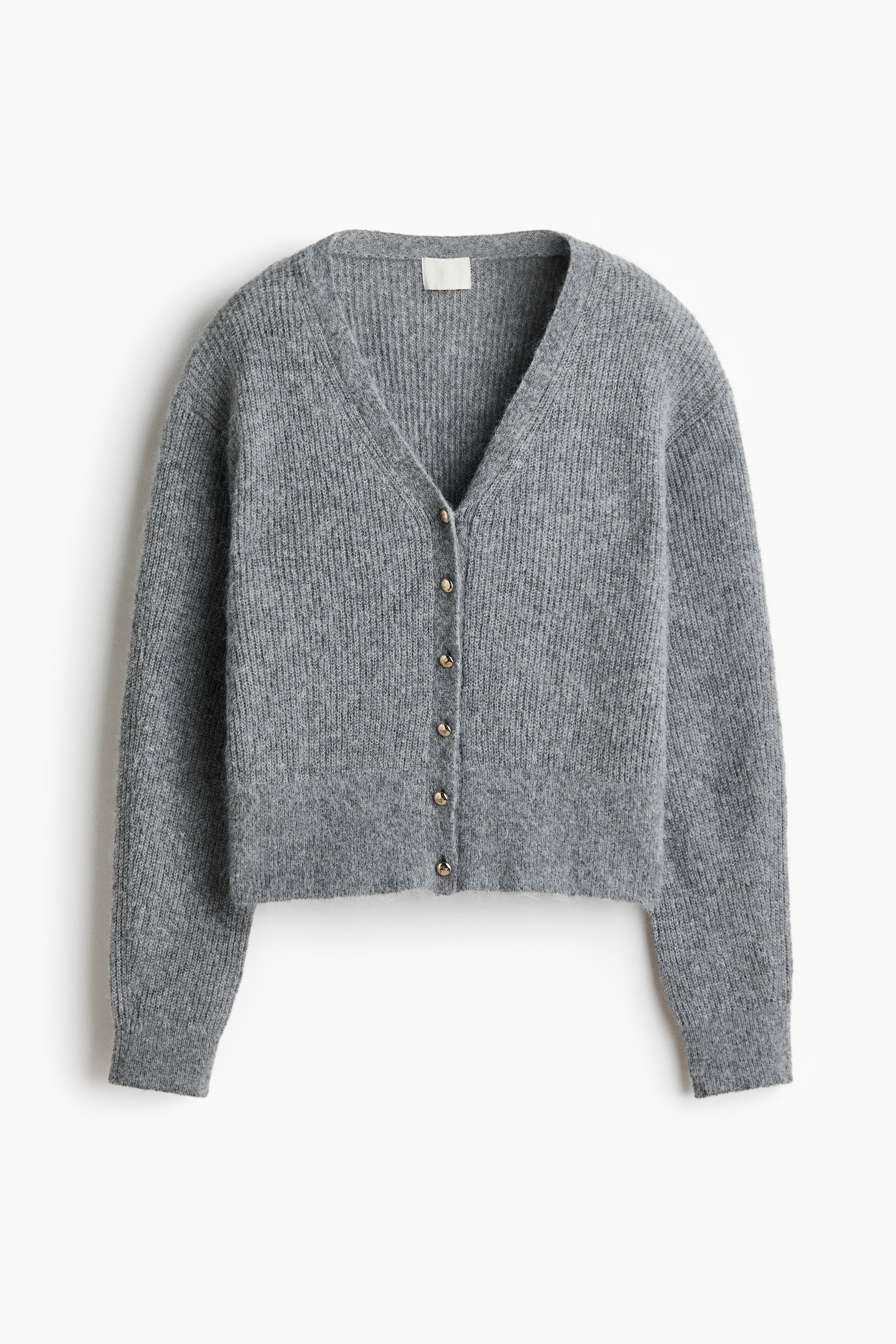 A short, grey rib-knit cardigan featuring a V-neckline and small buttons down the front is worn by the model. The cardigan, which has dropped shoulders and long sleeves with ribbed cuffs, is styled with dark, pleated pinstripe trousers.