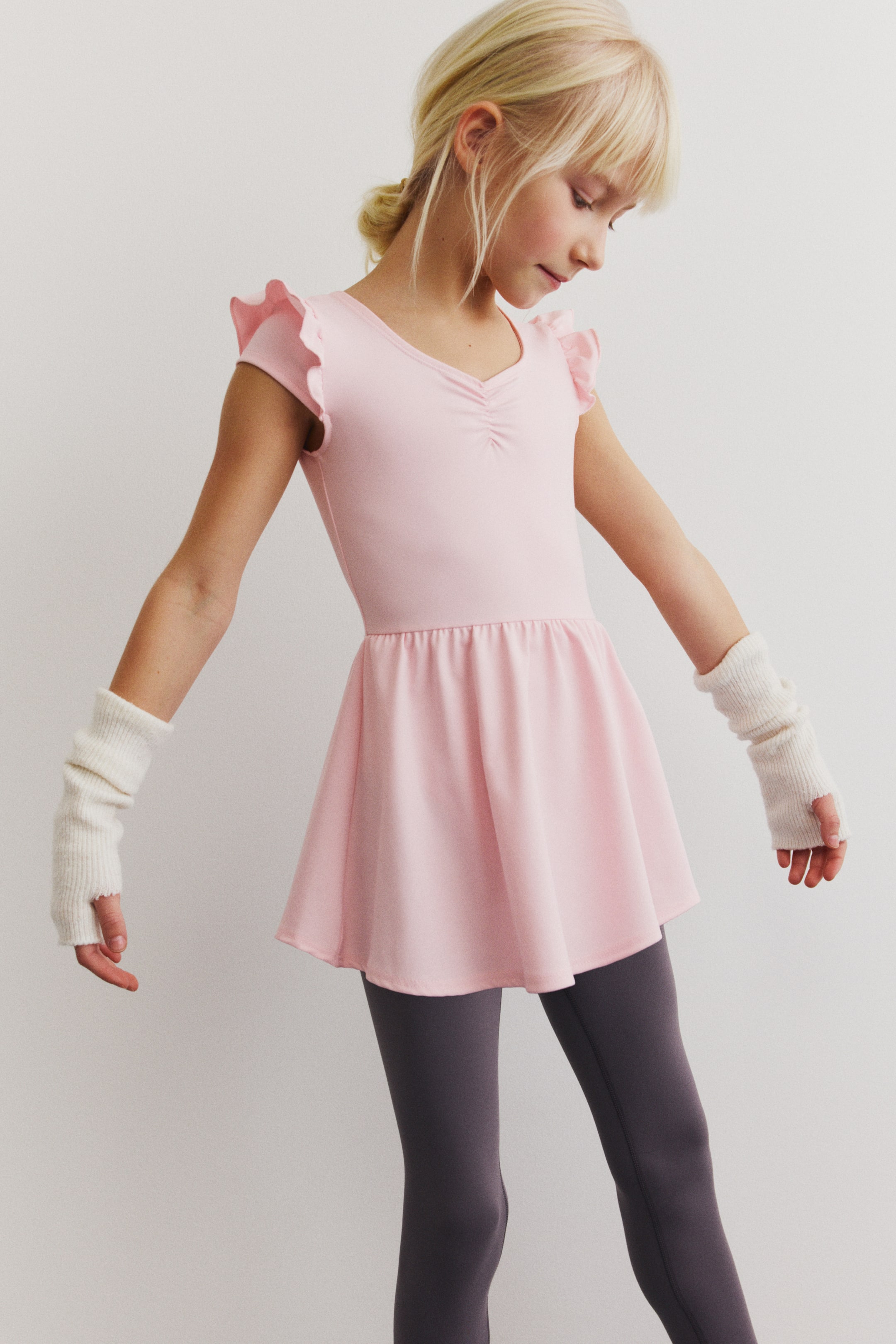 Größeres Bild ansehen: Ein rosa Trikot mit Rock verfügt über einen V-Ausschnitt mit vorne gerafften Details, kurze, mit Rüschen versehene Kappenärmel und einen angesetzten, ausgestellten Rock, der in der Taille gerafft ist.