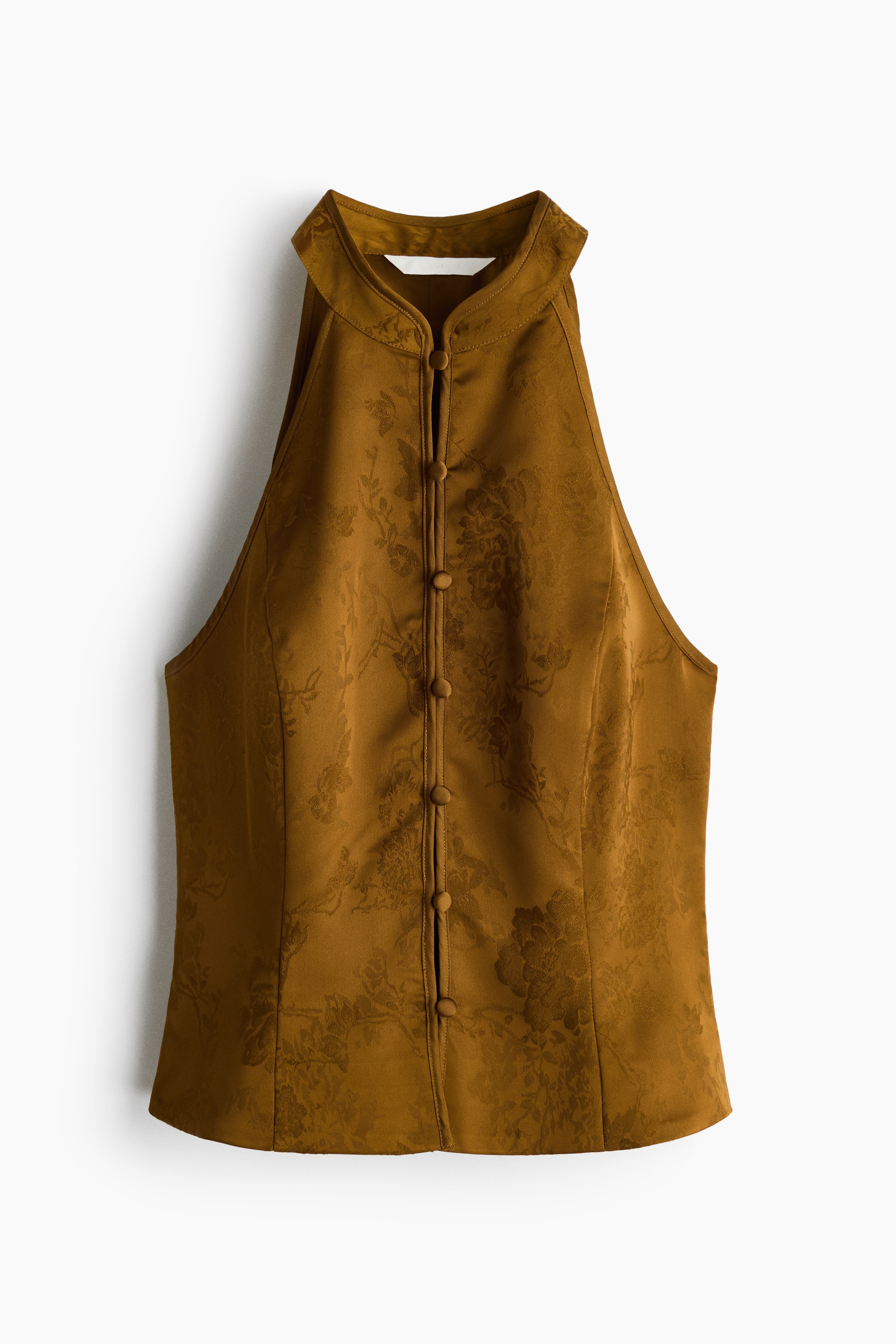 A short, fitted halterneck top in a golden-brown woven jacquard fabric is worn by the model. The top features a high band collar, an extra-narrow cut at the shoulders, princess seams, and a row of covered buttons down the front.