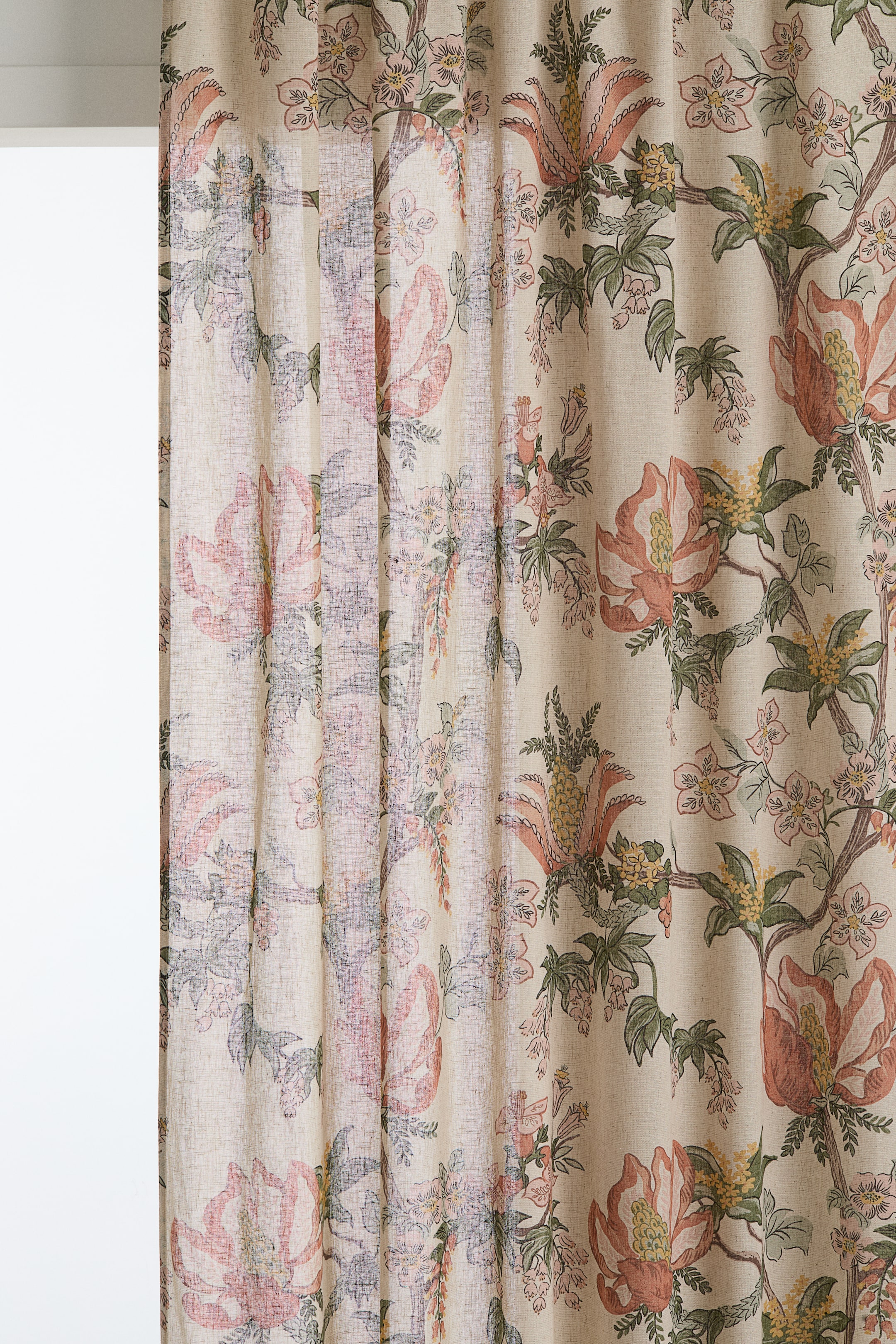 Vis større bilde: Et gardinpanel viser et heltrykt blomstermønster på et lyst, teksturert vevd stoff. Store, stiliserte blomster i nyanser av fersken, rosa og lilla, sammen med grønne blader og gule detaljer, dekker materialet, som henger i myke, vertikale folder og ser ut til å virke lysdiffuserende.
