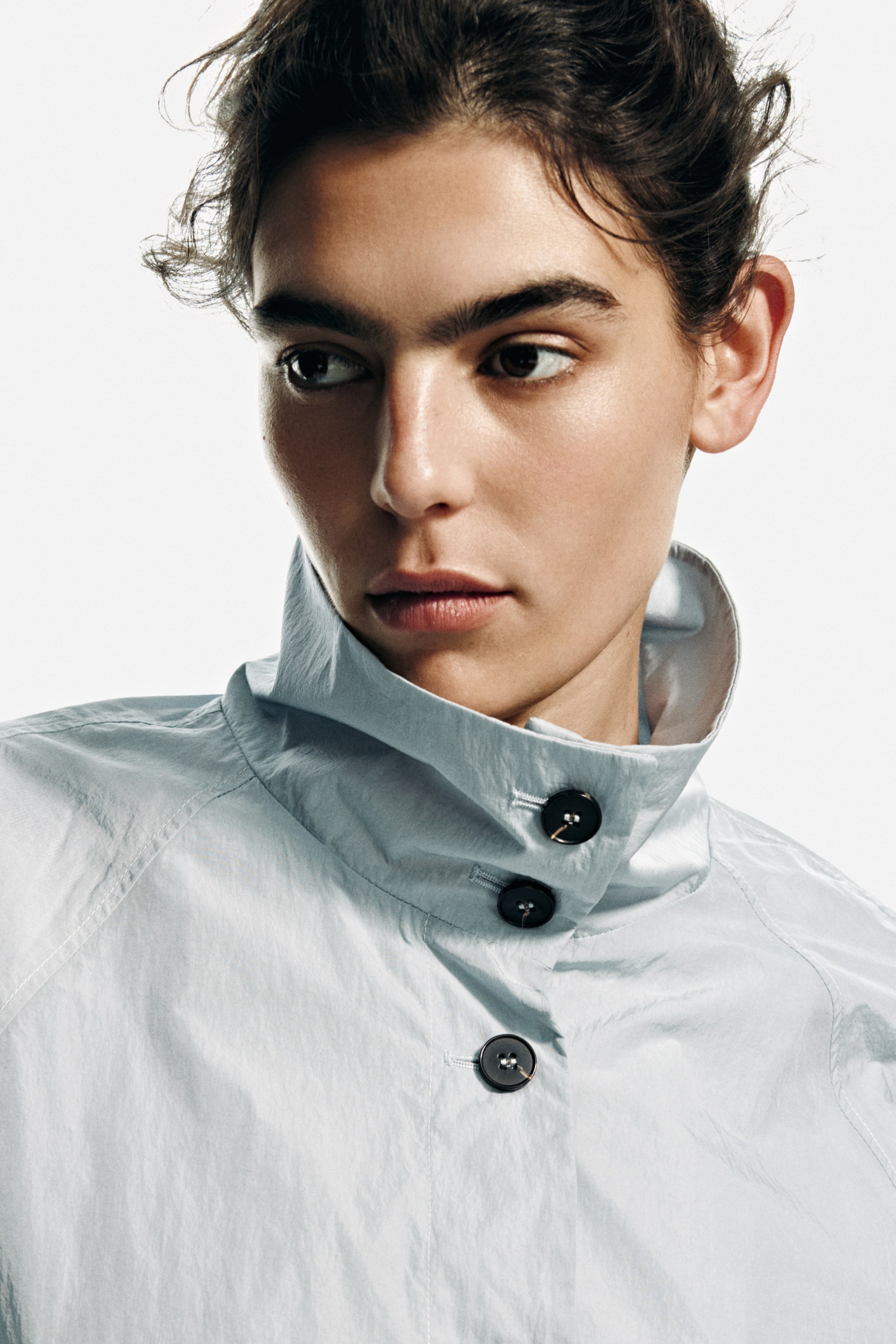 View larger image: This light blue-gray garment features a high standing collar, fully buttoned with three dark, round buttons on its front placket, and showcases a subtly shimmering, lightweight fabric from a slight left-facing angle.