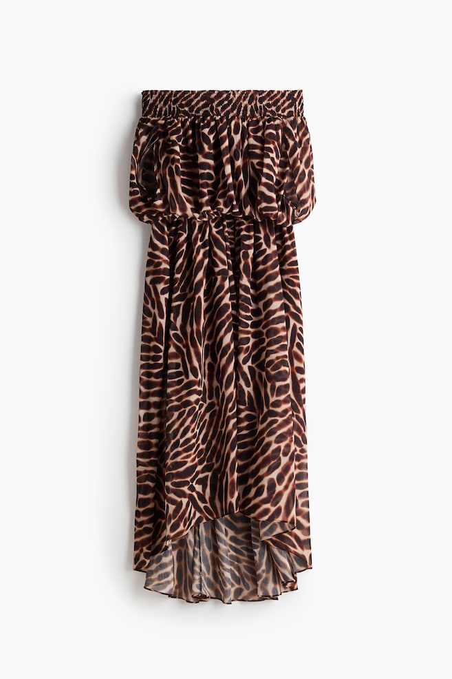 The dress is showcased from the front, featuring a brown and beige animal print throughout. It is crafted with a shirred, strapless bodice and an elasticated waist, flowing into a high-low hemline with a semi-sheer skirt. - 1