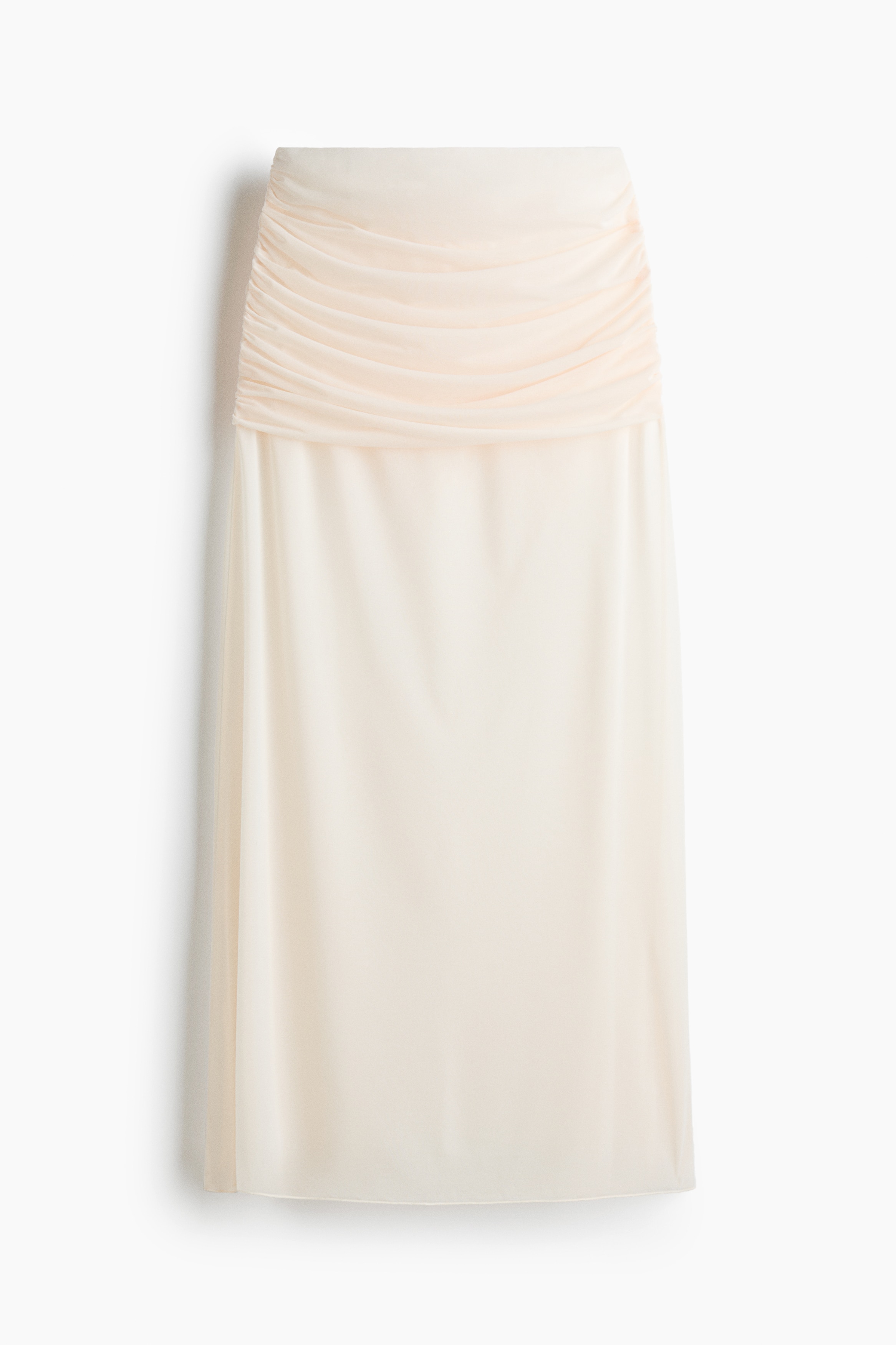 A brown jersey maxi skirt featuring a ruched, gathered waist with a draped effect is being worn by the model, who is holding the flared, semi-sheer hem to the side. The skirt is paired with a matching draped brown sleeveless top.