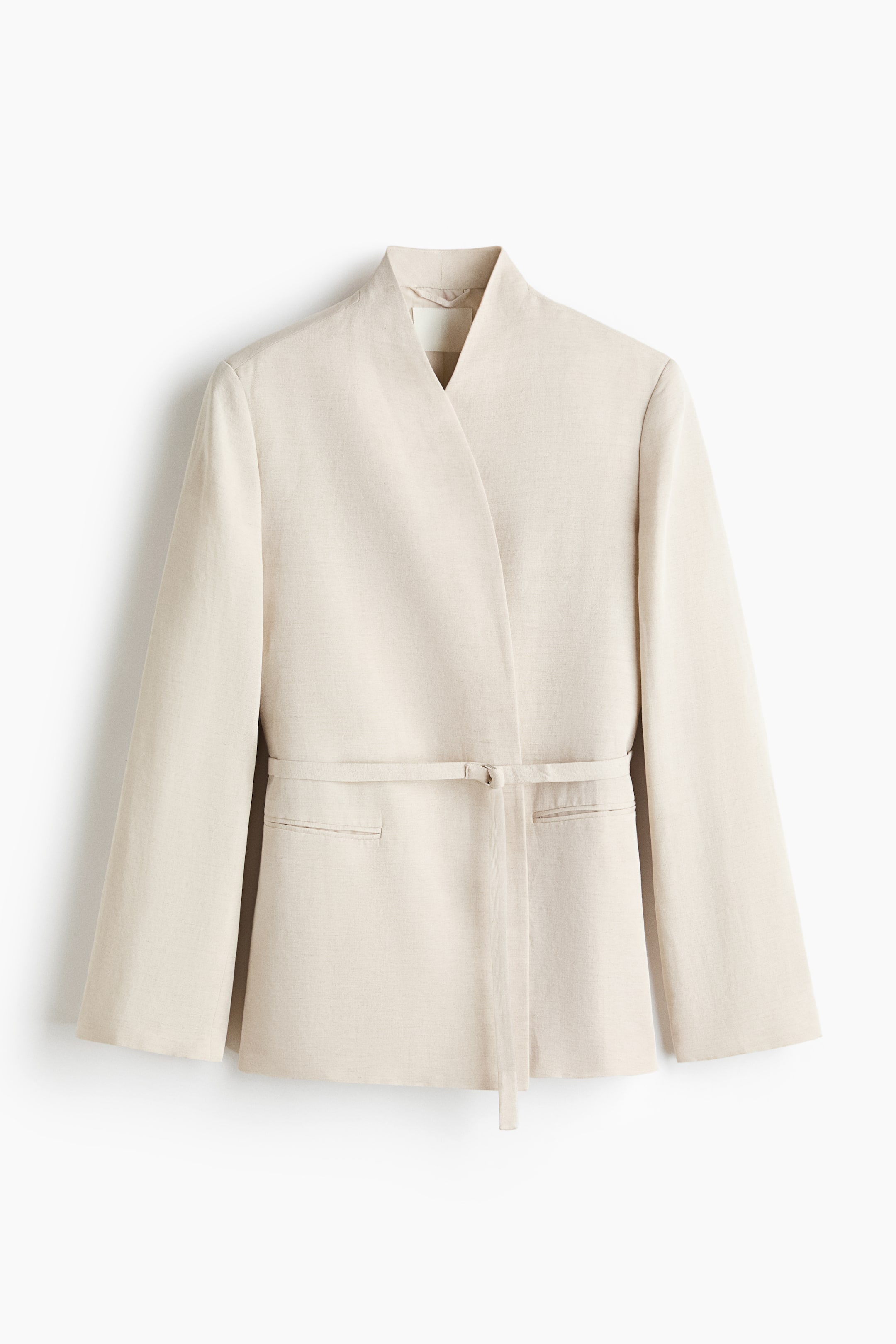 View larger image: A light beige wrap-style jacket is showcased at the front, featuring a collarless V-neckline and long sleeves. A matching self-fabric belt cinches the waist, with two patch pockets visible below the belt.