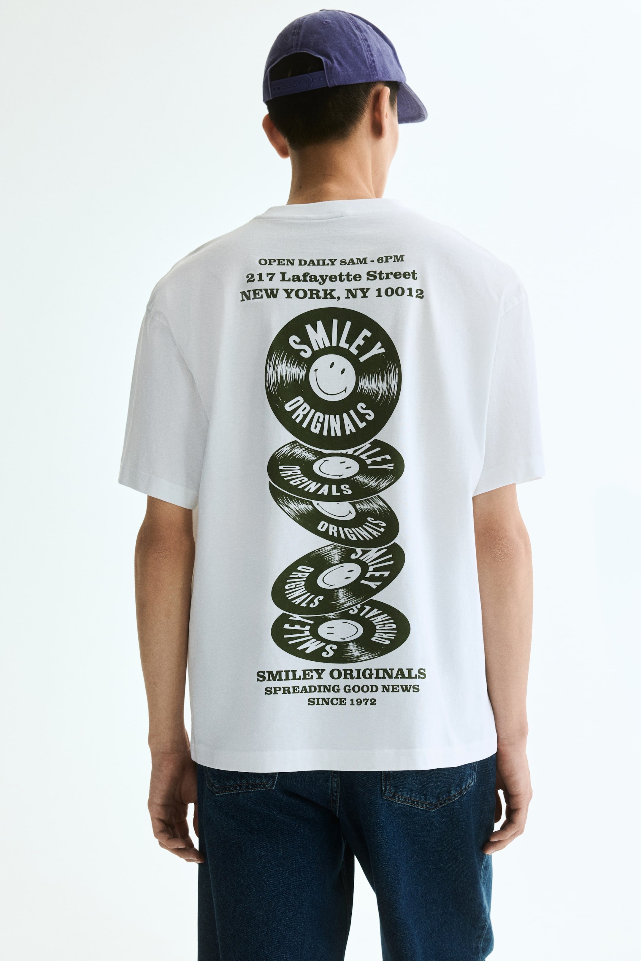 View larger image: This soft, printed midweight cotton jersey t-shirt showcases a relaxed fit with dropped shoulders and a round neckline accented by a narrow trim. On the back, it features a large dark green graphic with text at the top and bottom, along with a vertical stack of five vinyl records, each adorned with a smiley face and the 'Smiley Originals' text.