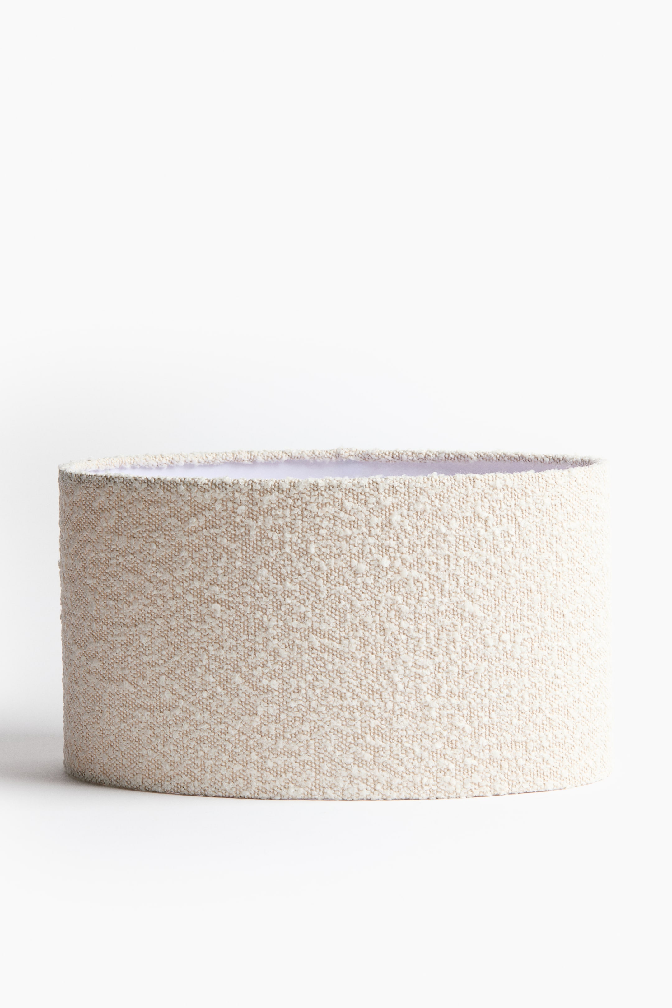 View larger image: A drum lampshade is standing upright, showcasing its light beige textured exterior fabric with subtle darker flecks. Its white interior lining is visible along the top rim.