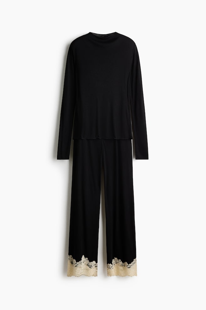 Ein schwarzes Pyjama-Set aus Rippjersey ist von vorne zu sehen und besteht aus einem Langarmshirt mit Rundhalsausschnitt. Die dazu passende Hose mit weitem Bein ist an den SÃ¤umen mit kontrastierender cremefarbener Spitzenborte versehen. - 1