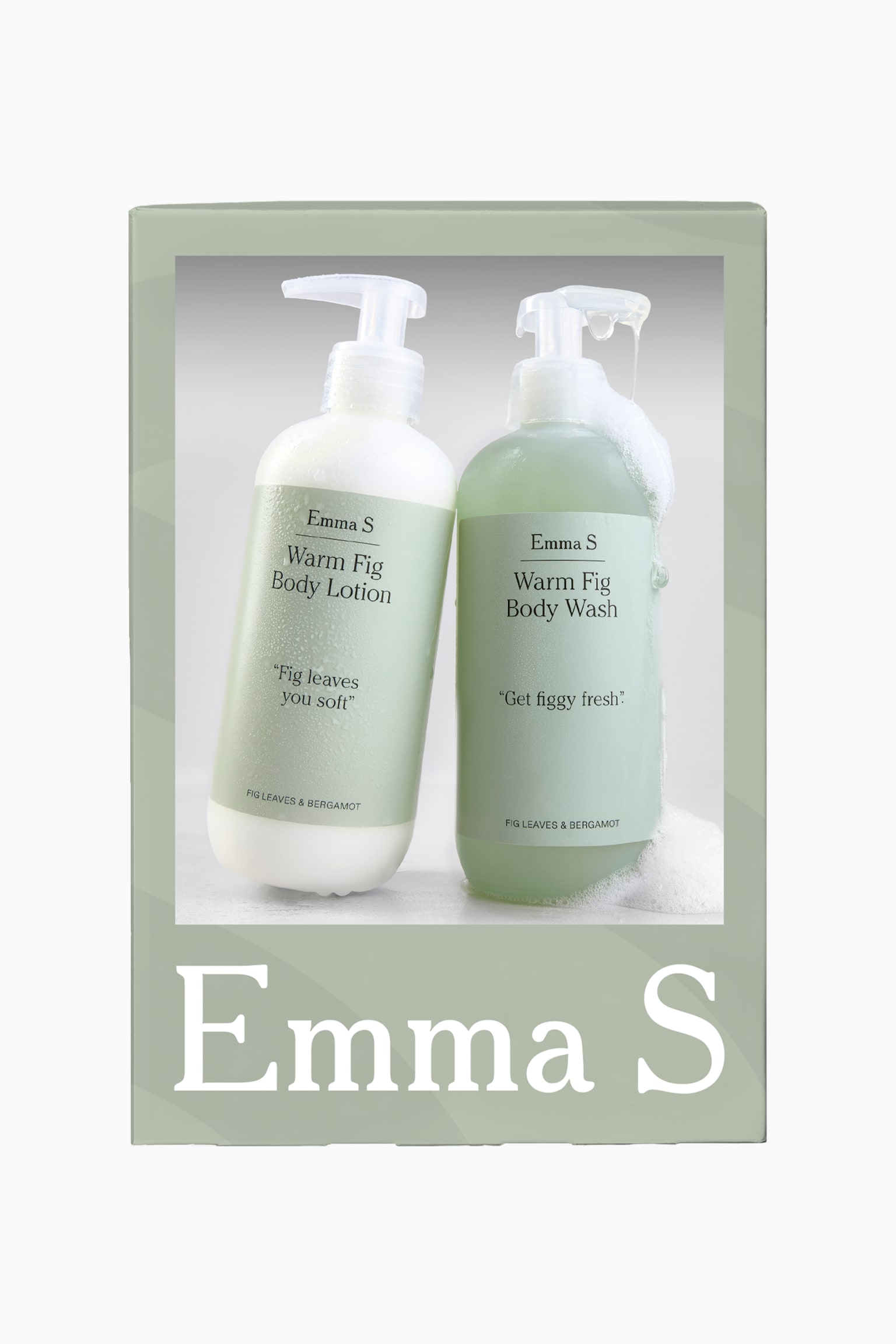 En salviagrön presentask visar en central bild av två pumpflaskor som står sida vid sida: en flaska med "Warm Fig Body Lotion" med kondensdroppar till vänster, och en flaska med "Warm Fig Body Wash" med vit tvålskum som rinner ner längs sidan till höger. Båda flaskorna är vända framåt och visar ljusgröna etiketter med varumärket "Emma S" samt doftnamnet "Fig Leaves & Bergamot". - 1
