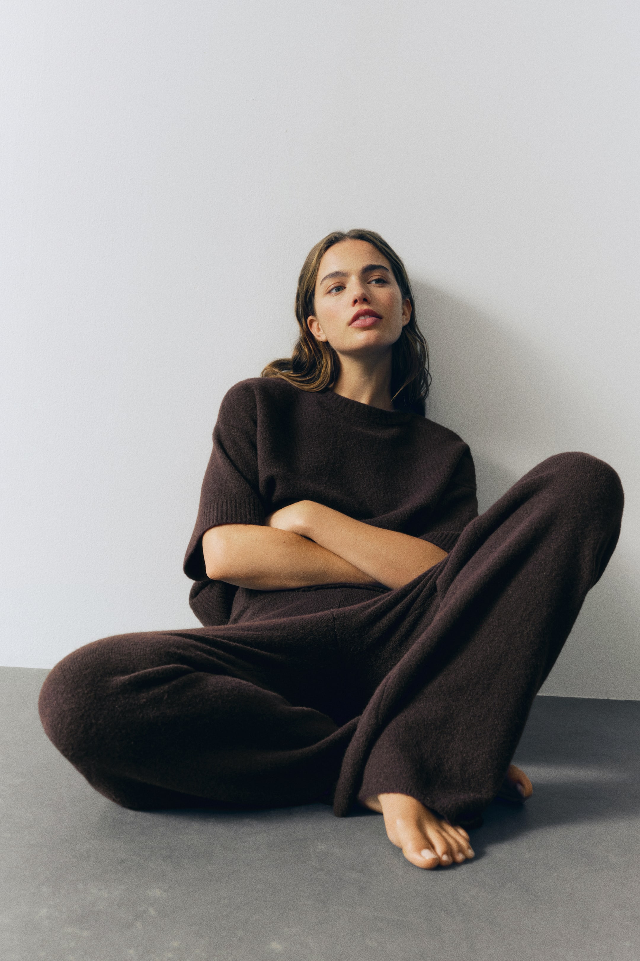 Agrandir l'image: Pantalon ajusté marron foncé, confectionné dans un tricot doux contenant de la laine, avec une taille élastiquée dissimulée. Le pantalon présente des jambes larges avec des côtes étroites aux ourlets.