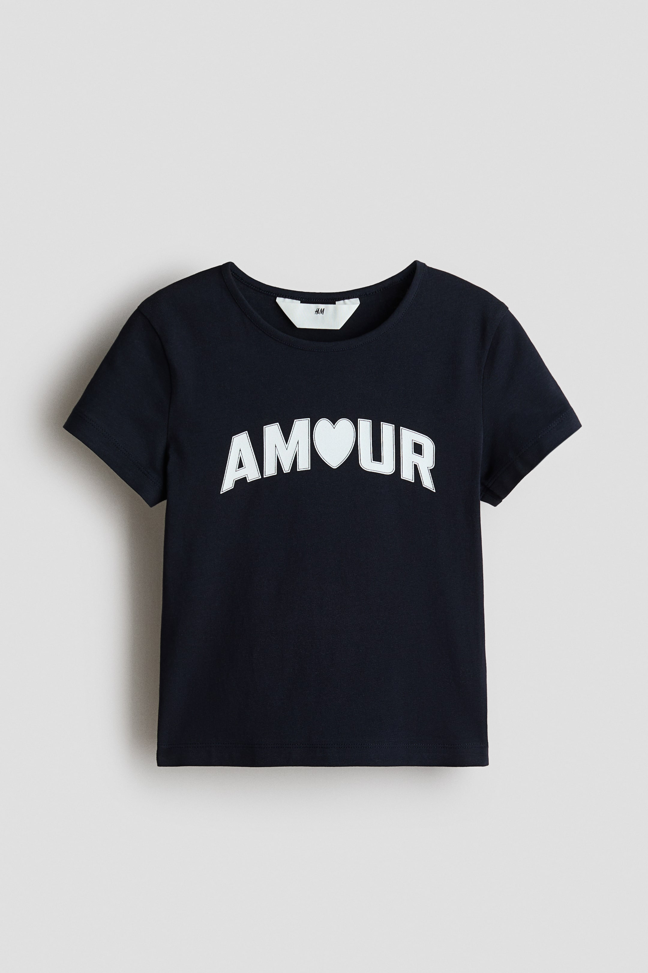 View larger image: A short-sleeved top is shown from the FRONT, featuring a round neckline and a white “AMOUR” print with a heart symbol replacing the letter ‘O’.